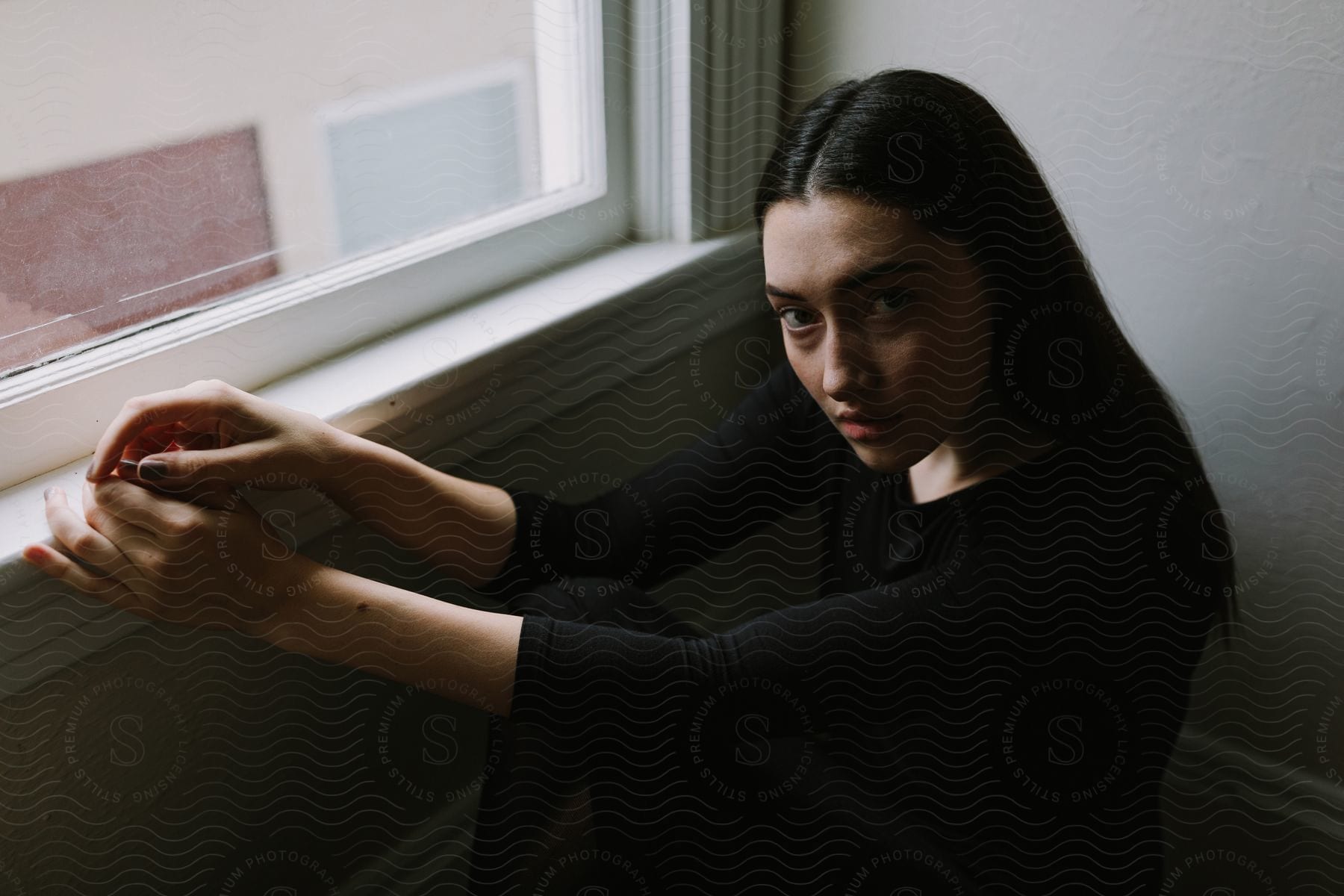 Dark haired woman dressed in black sitting on the floor next to a window