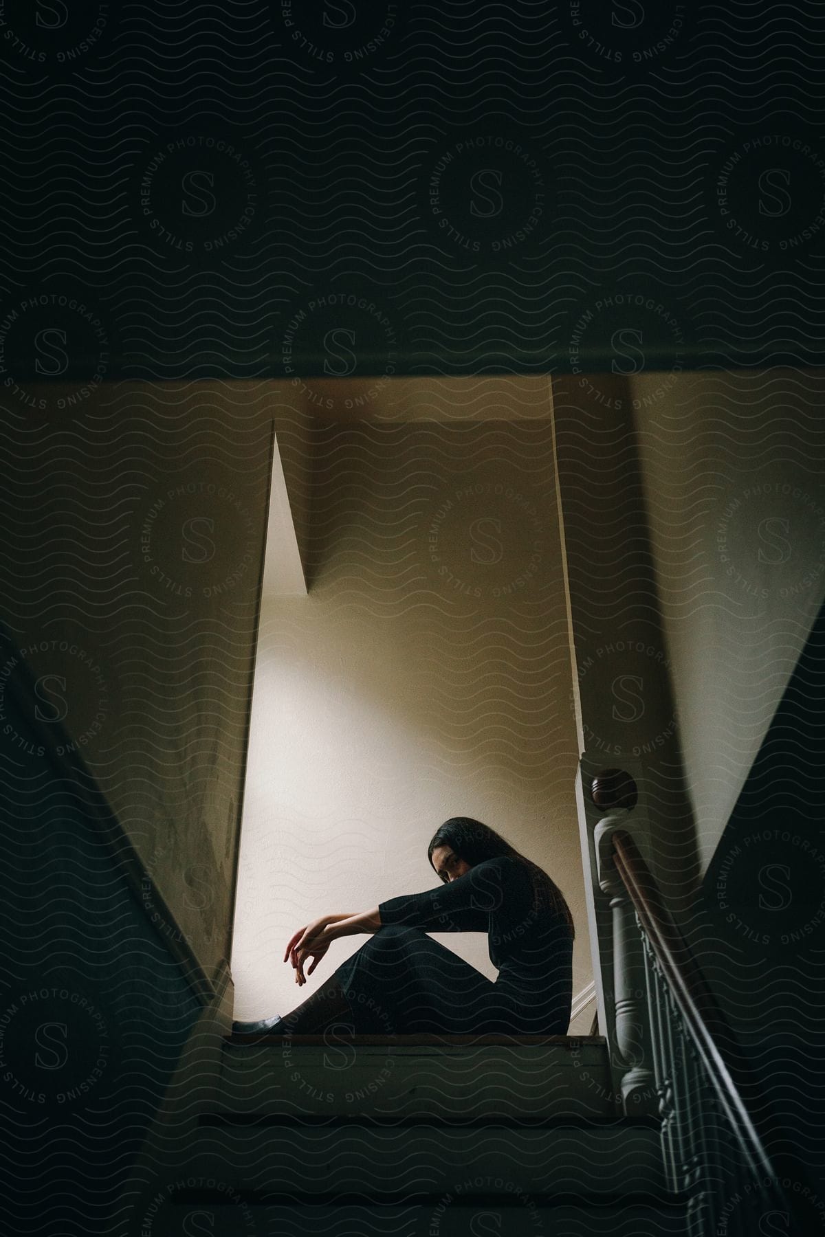 A womans silhouette sitting at the top of a staircase indoors