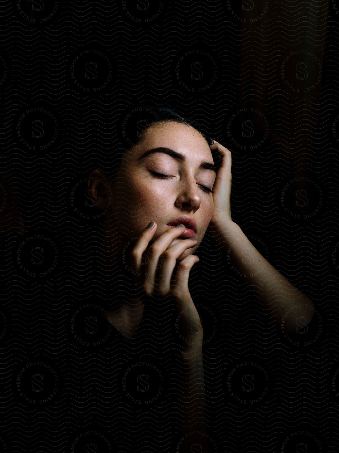 Woman with closed eyes in the dark one hand on head other hand covering face