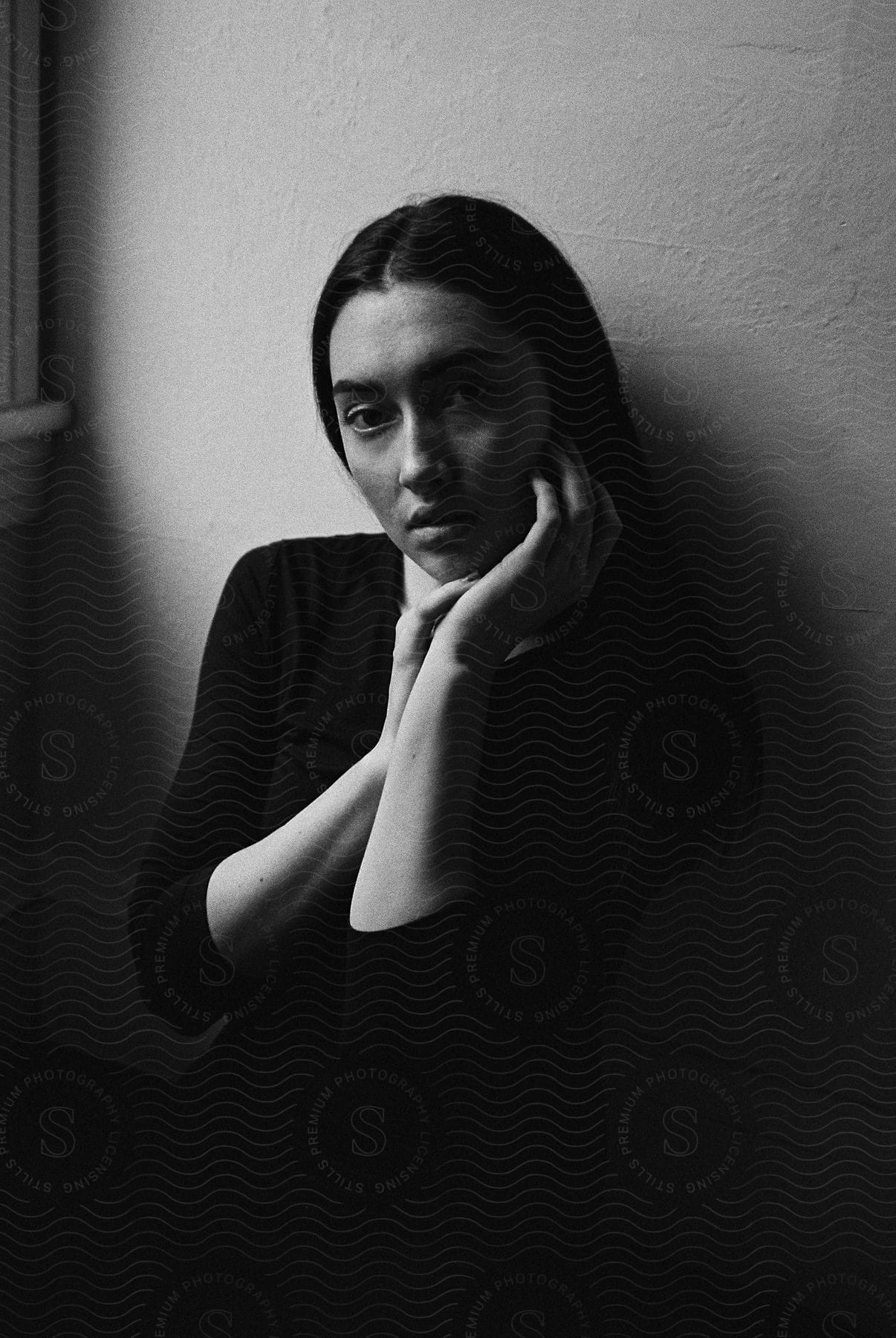 A woman sitting against a wall with her hands on her face in black and white