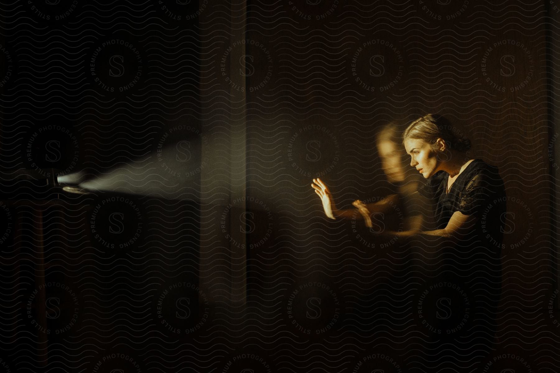 A woman dressed in black gesticulating towards a light source in a double exposure