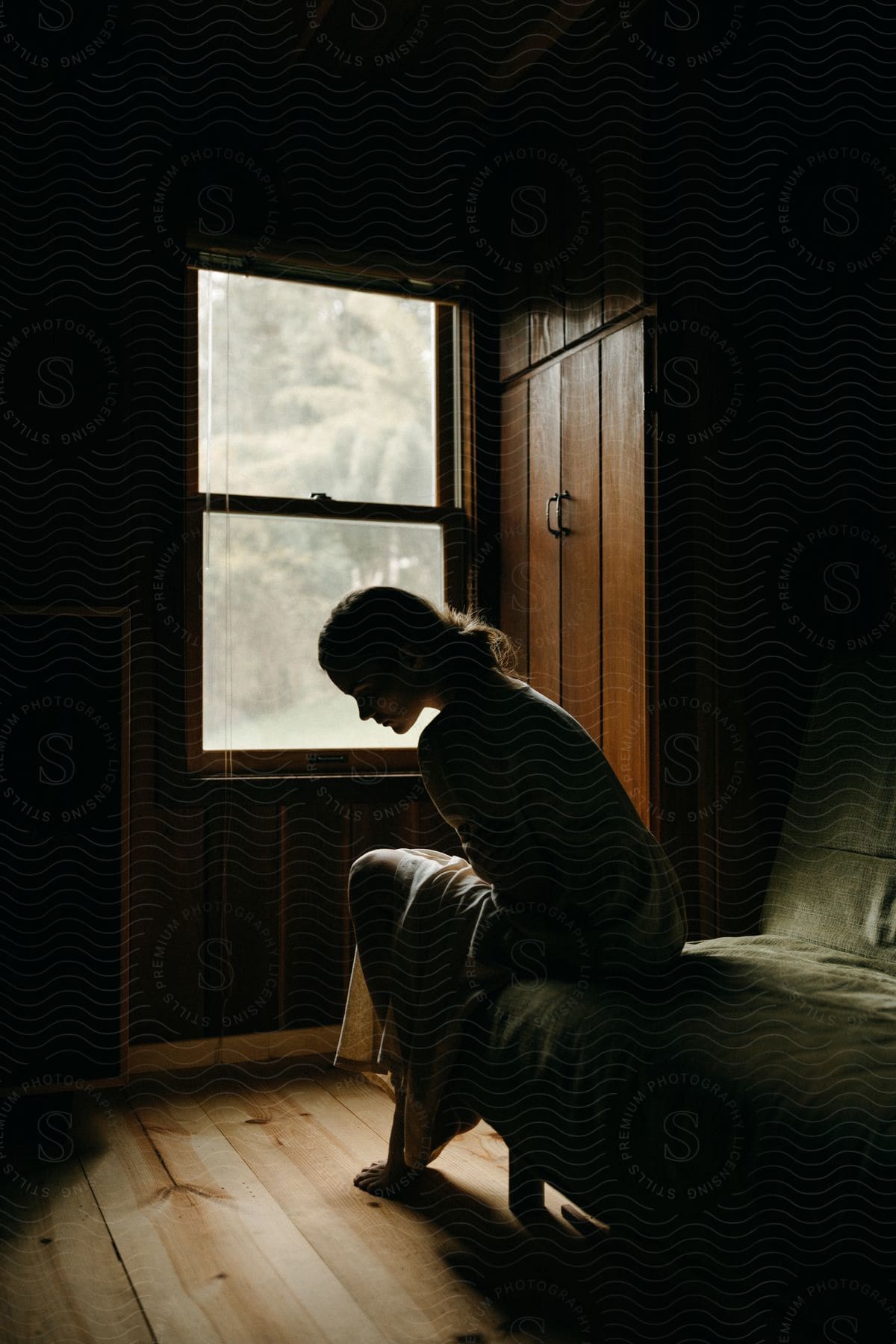 A young lady standing alone in a dark room illuminated by a subtle light source