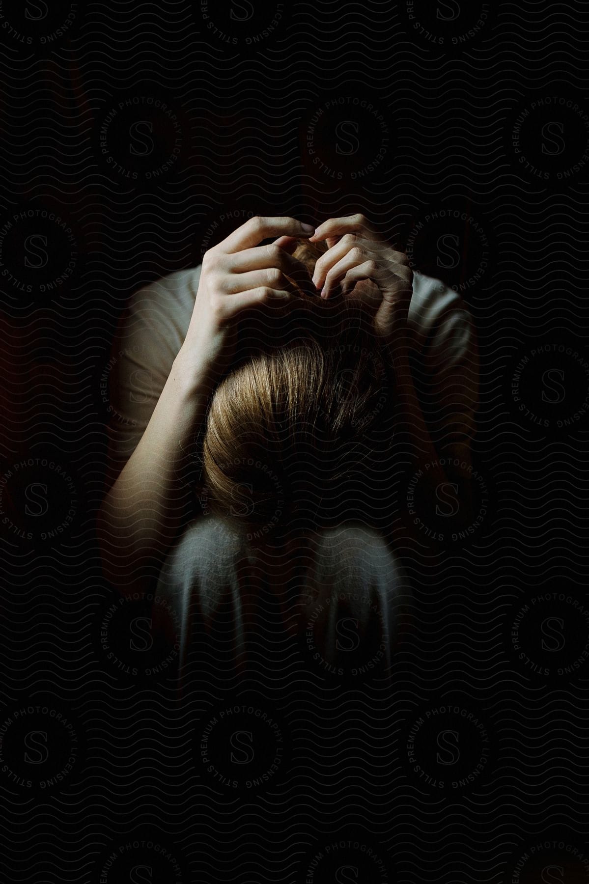 Sad woman sitting with her face covered hugging her knees in a lowlit interior space at night