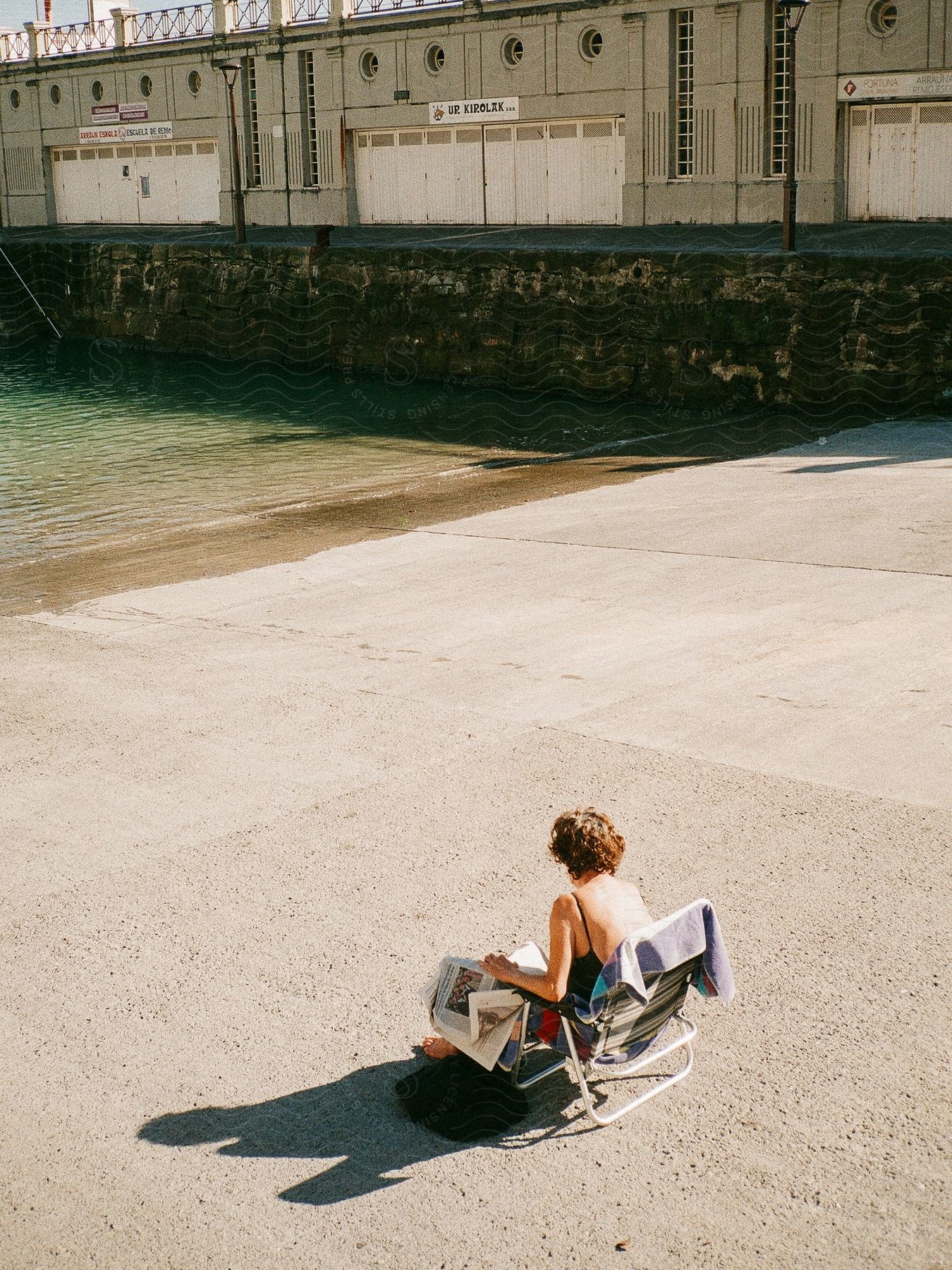 A person sitting on a chair near the shoreline reading