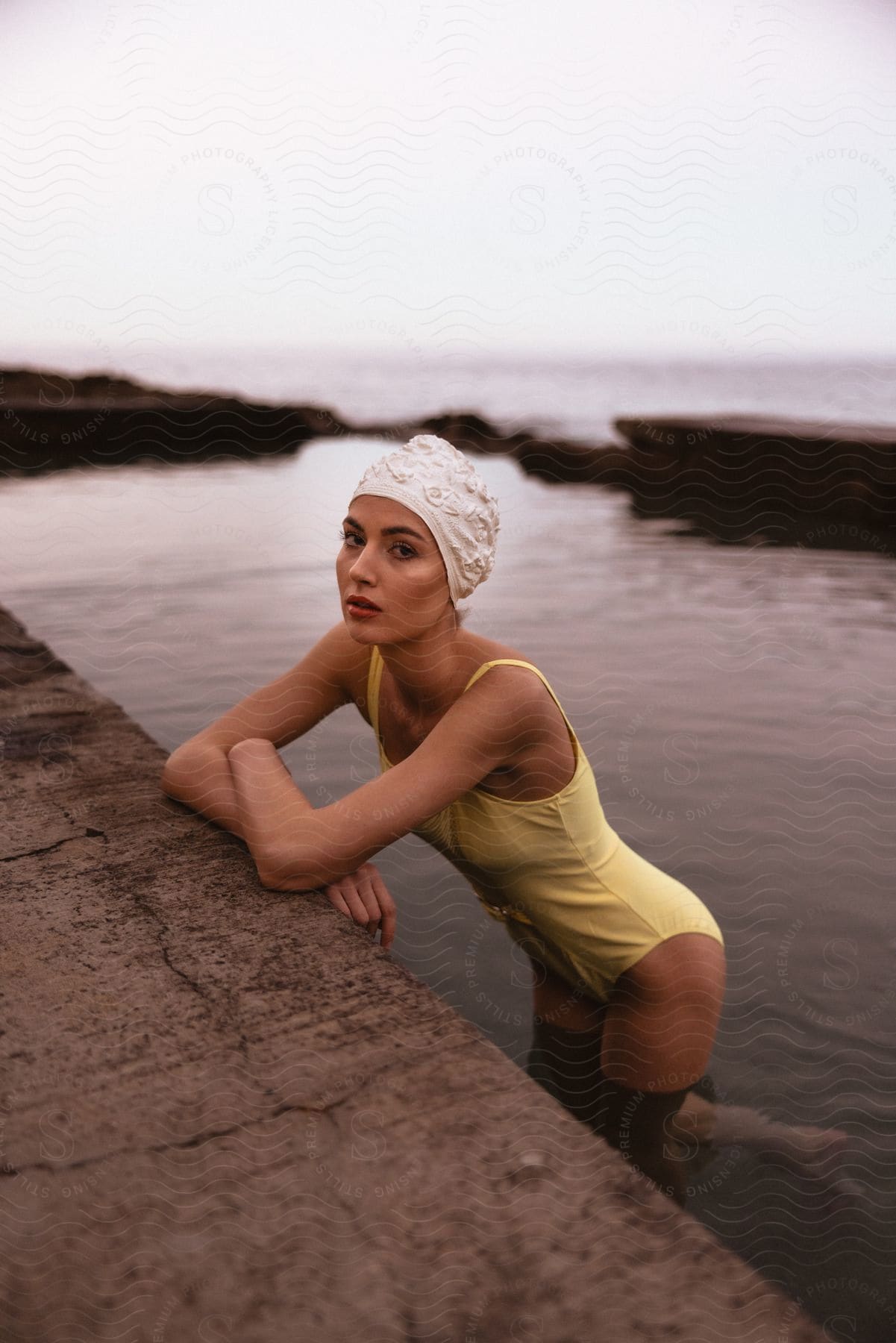 A woman in a yellow bathing suit leans on a concrete structure in thighdeep water