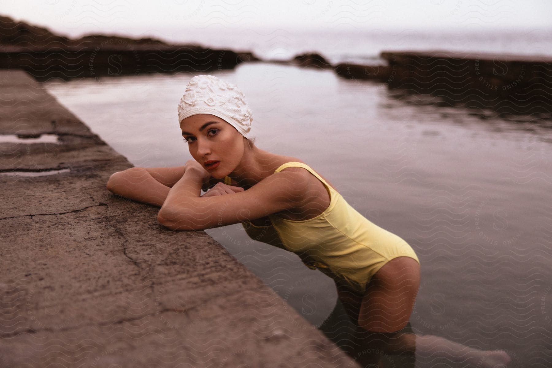 A young woman wearing a vintage swimsuit reclined on a pier looking at the camera