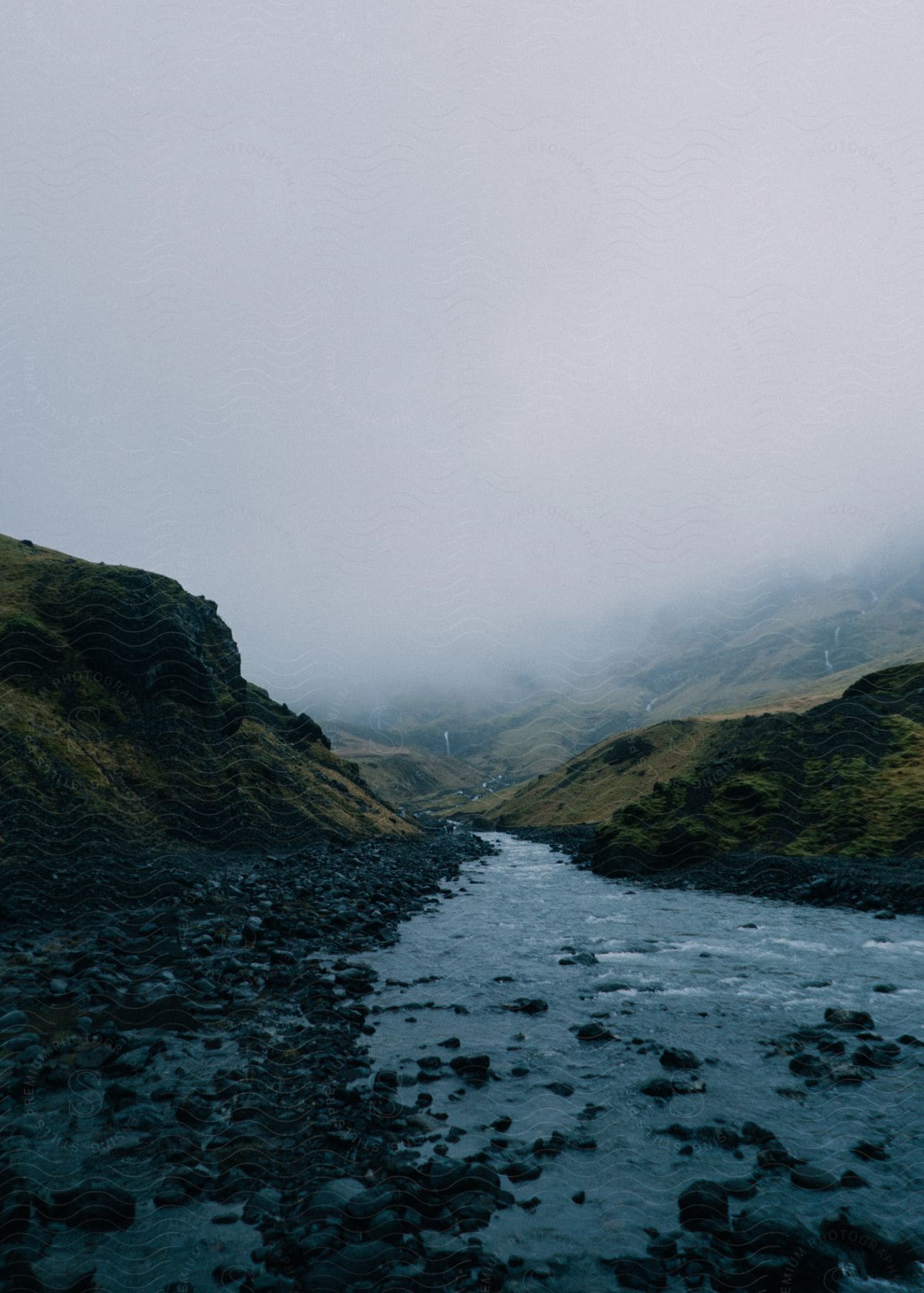 A stream runs between hills with fog in the sky