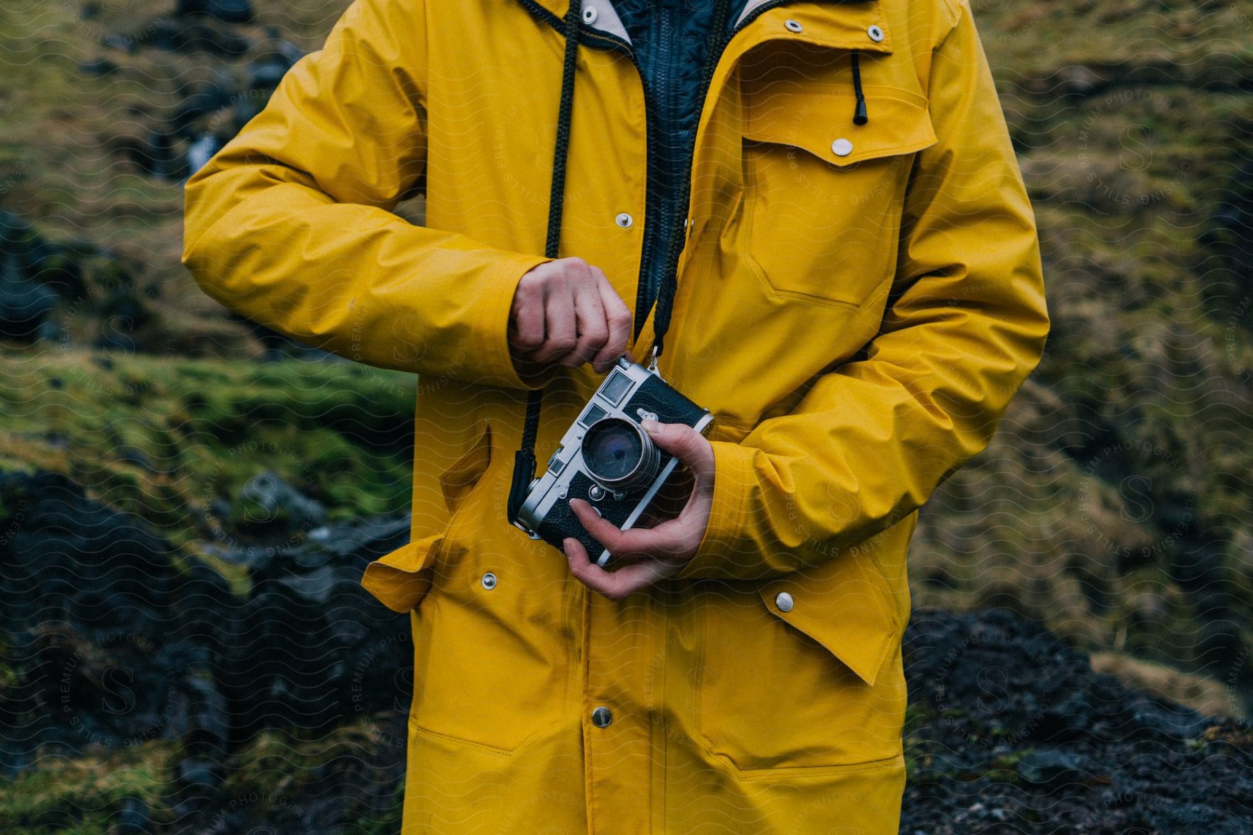 A person wearing a raincoat and holding a camera in a grassy field