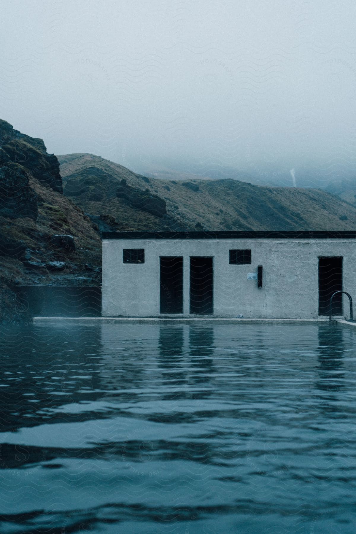 An industrial building rests on top of a dam in a lake surrounded by rocky hills on a misty day