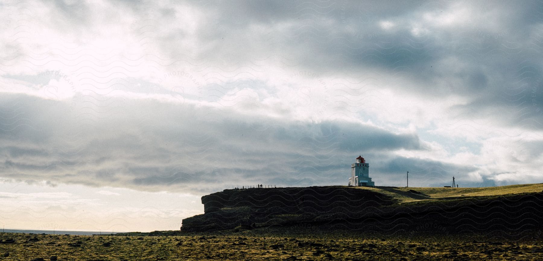 A lighthouse stands on a hill near the ocean under white clouds in the evening