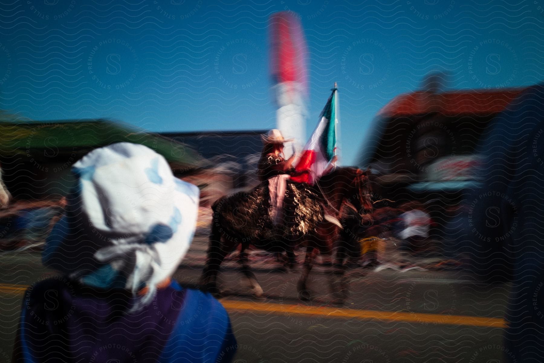 A blurry shot of a person riding a horse on the town streets carrying a mexican flag
