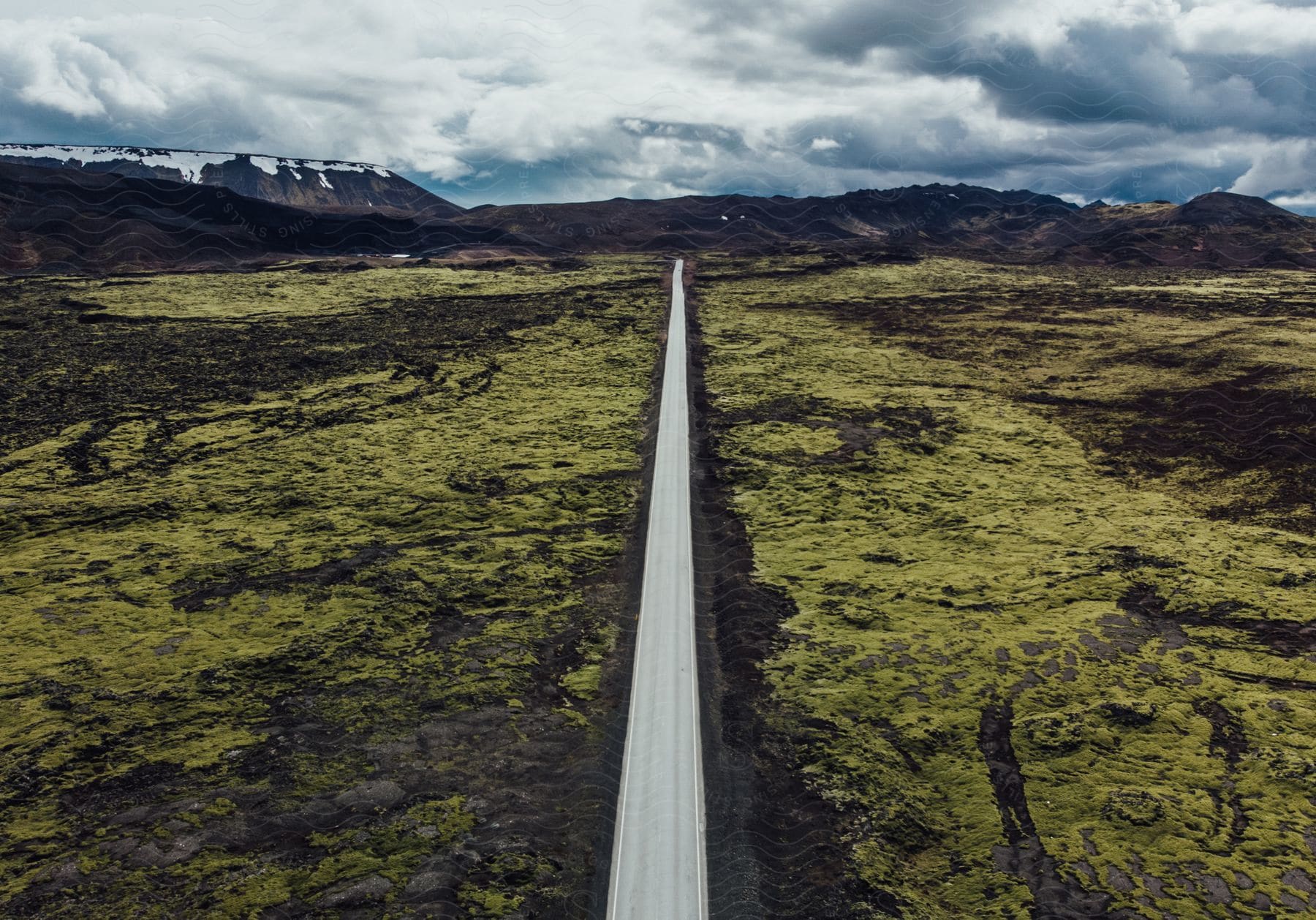 A highway cuts through tundra with a mountain range in the distance