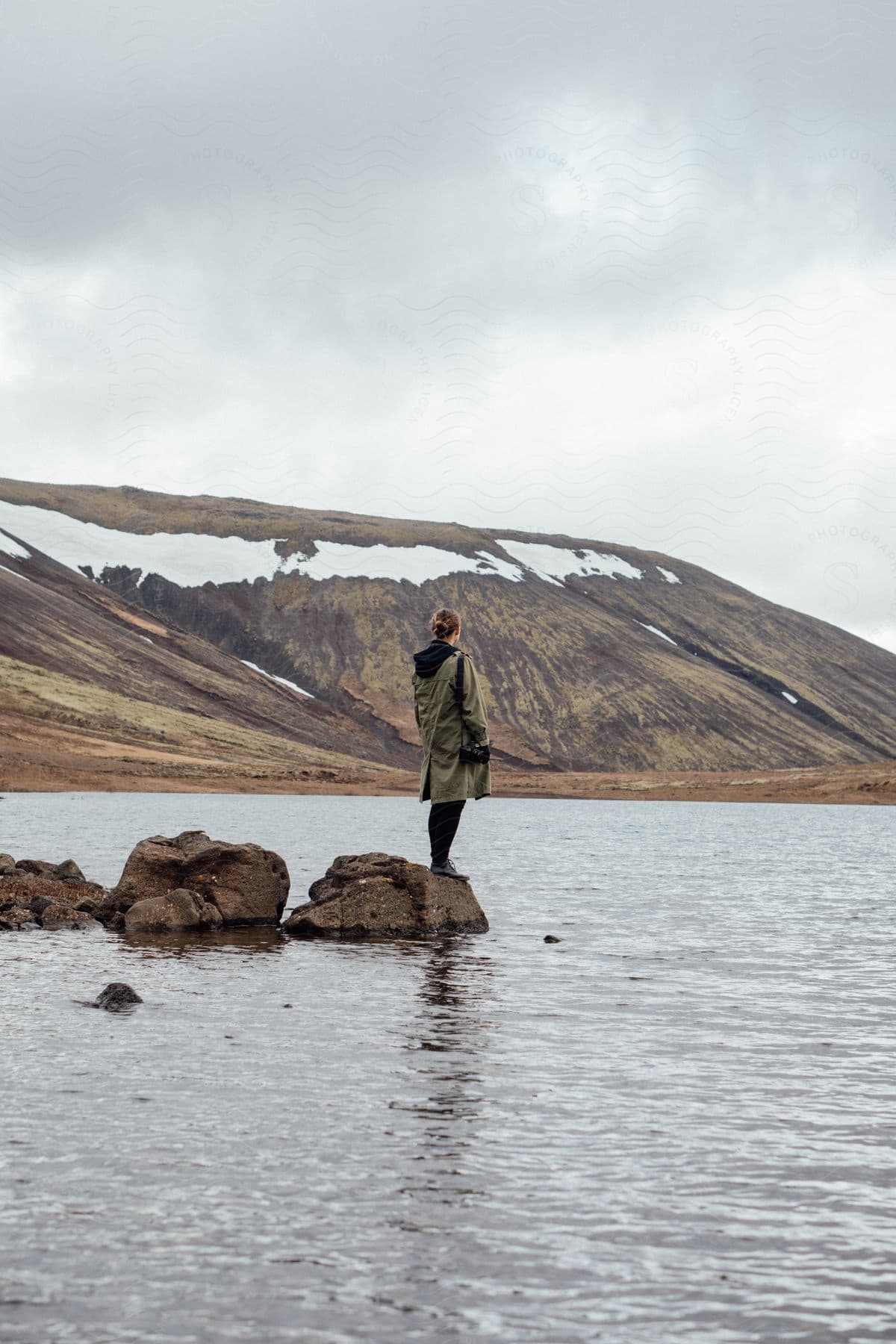 A female standing on a rock in a lake near a hillside