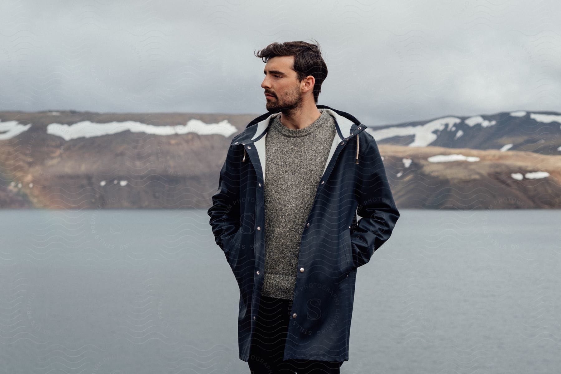 A male posing in front of a body of water and mountains during dusk or dawn