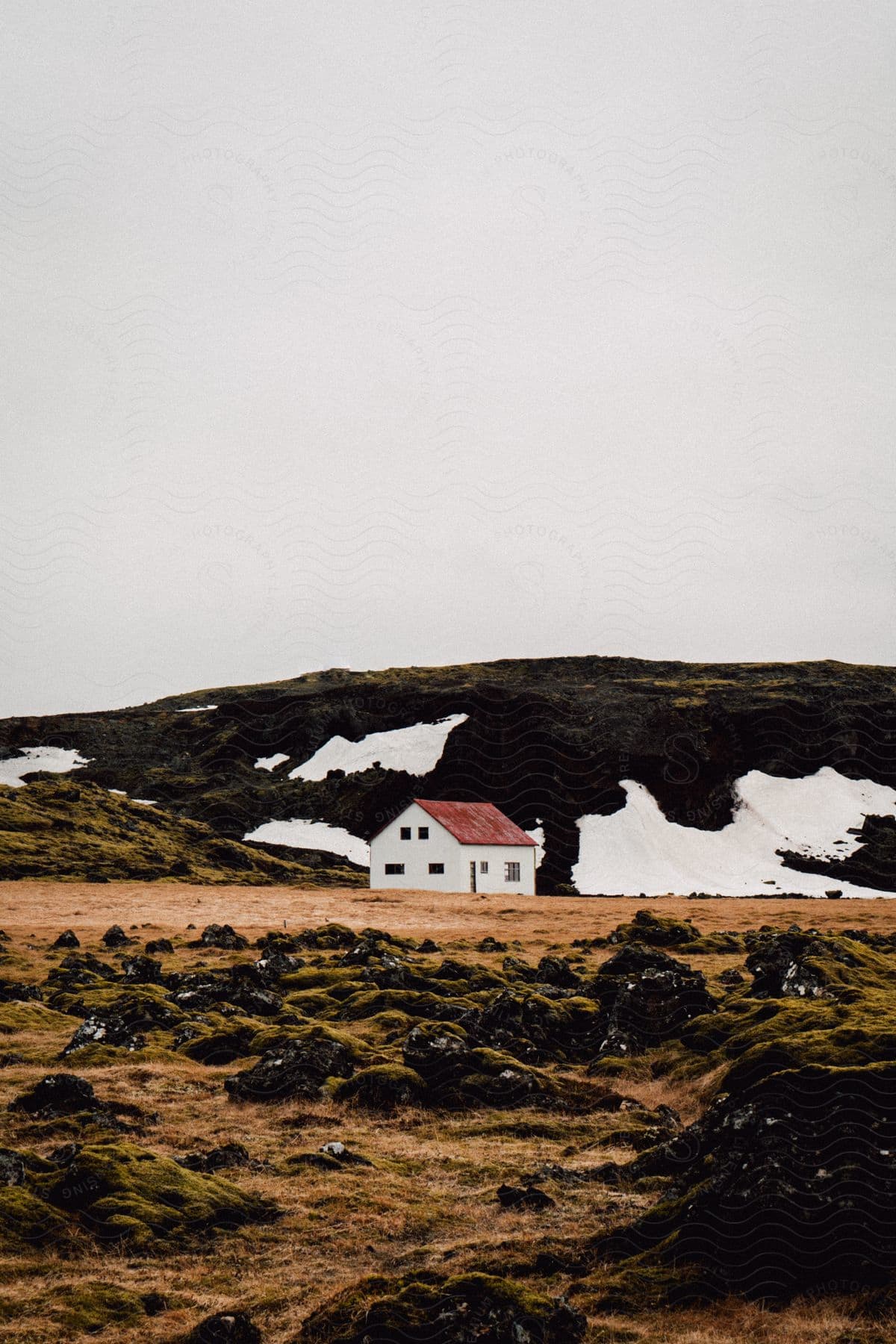 A white house with red roof near a hill covered with patches of snow on a cloudy day in iceland