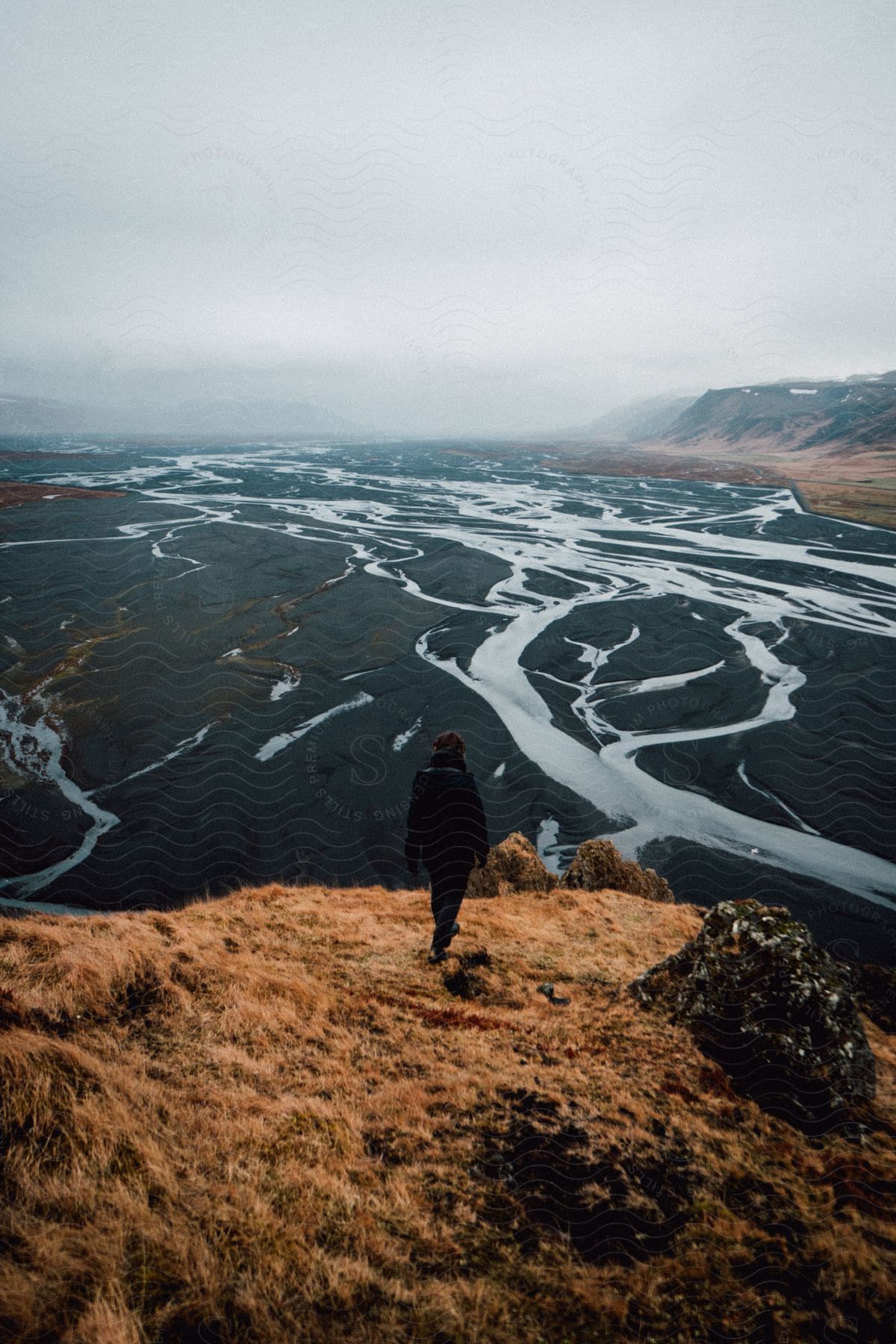 A person stands in the icelandic wilderness surrounded by mountains and water