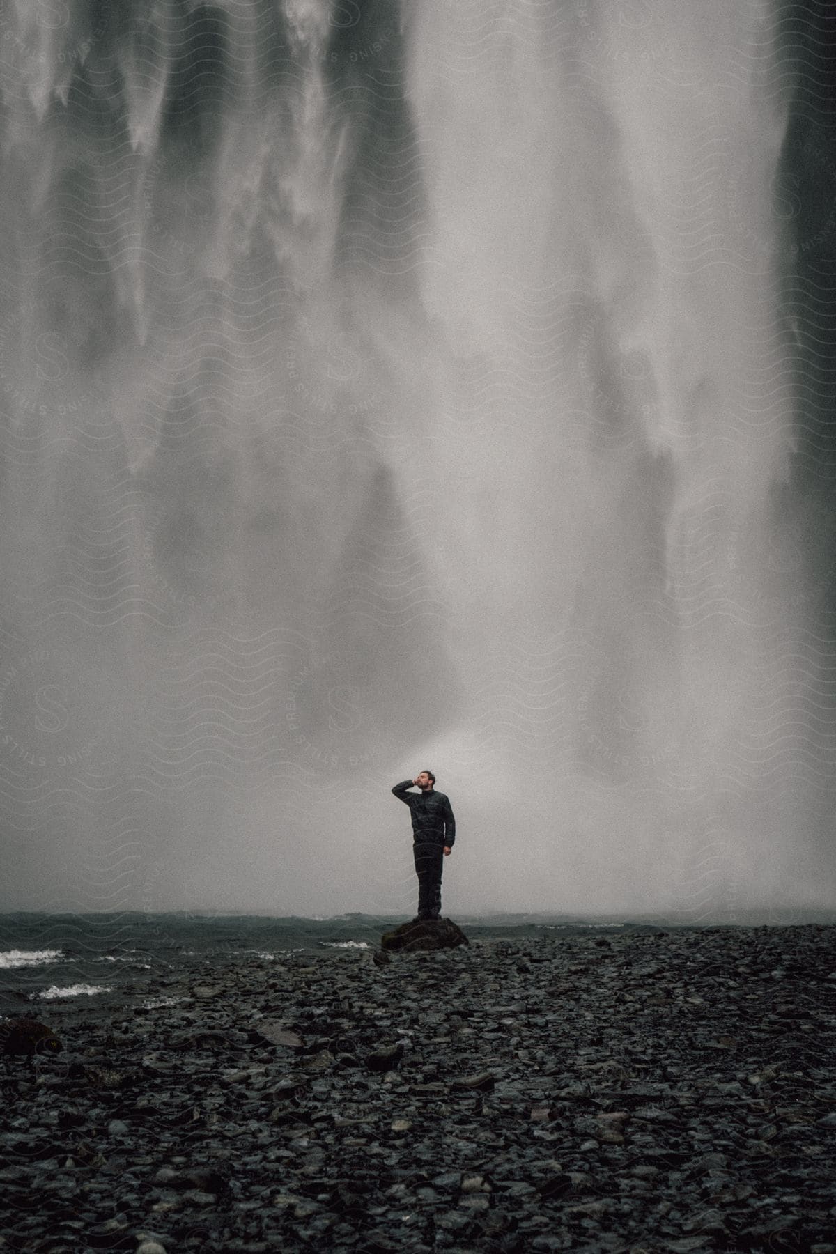 A man in black clothes standing with his back to a waterfall.