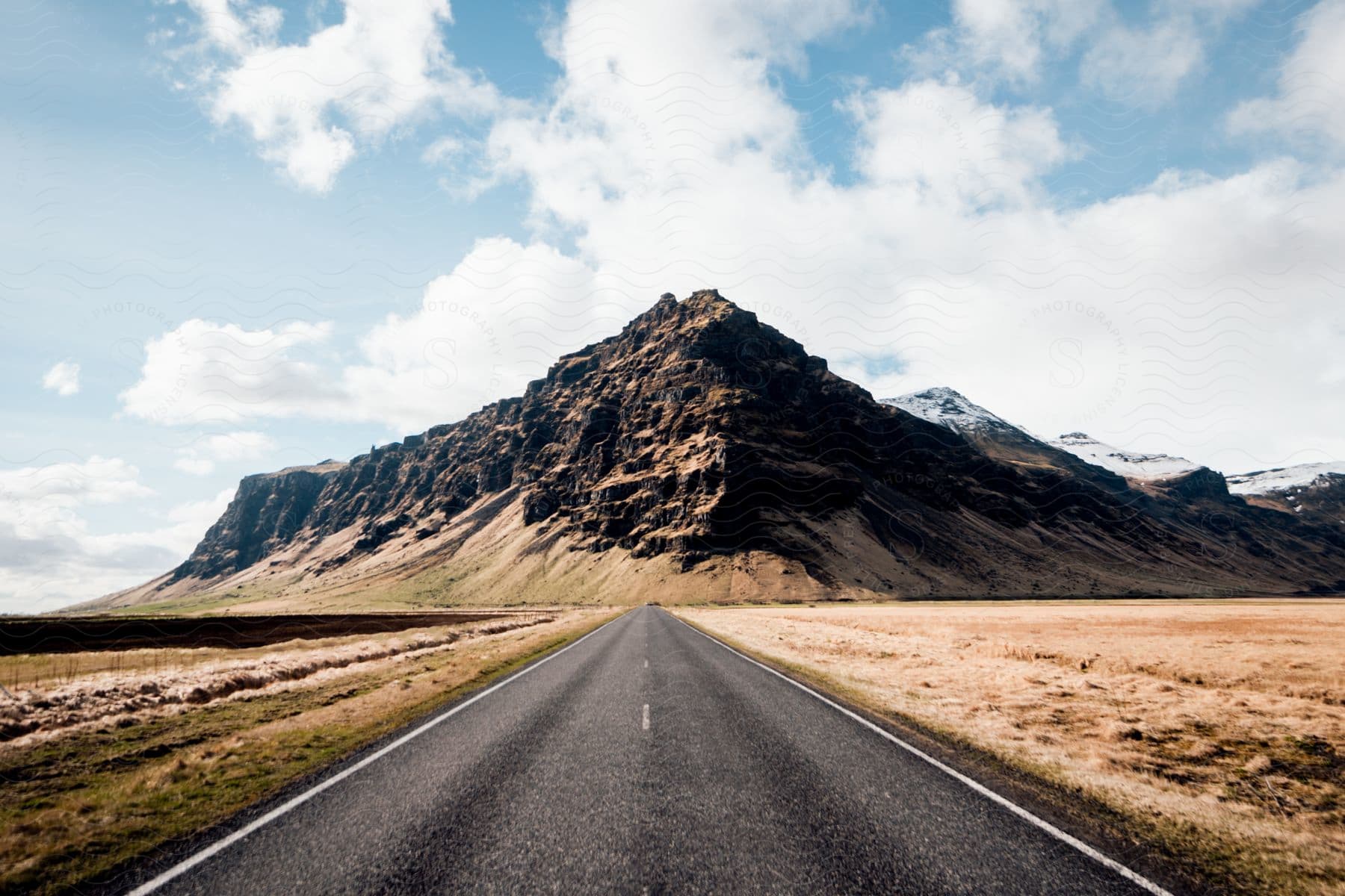 A road stretches alongside a mountain on a cloudy day