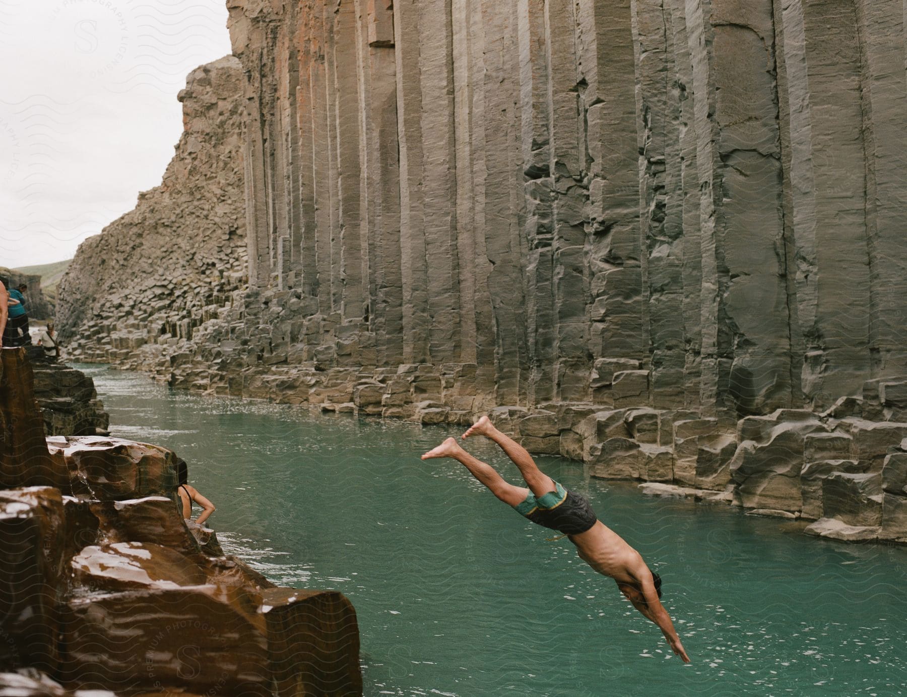 A man jumps in a river by a rocky cliff