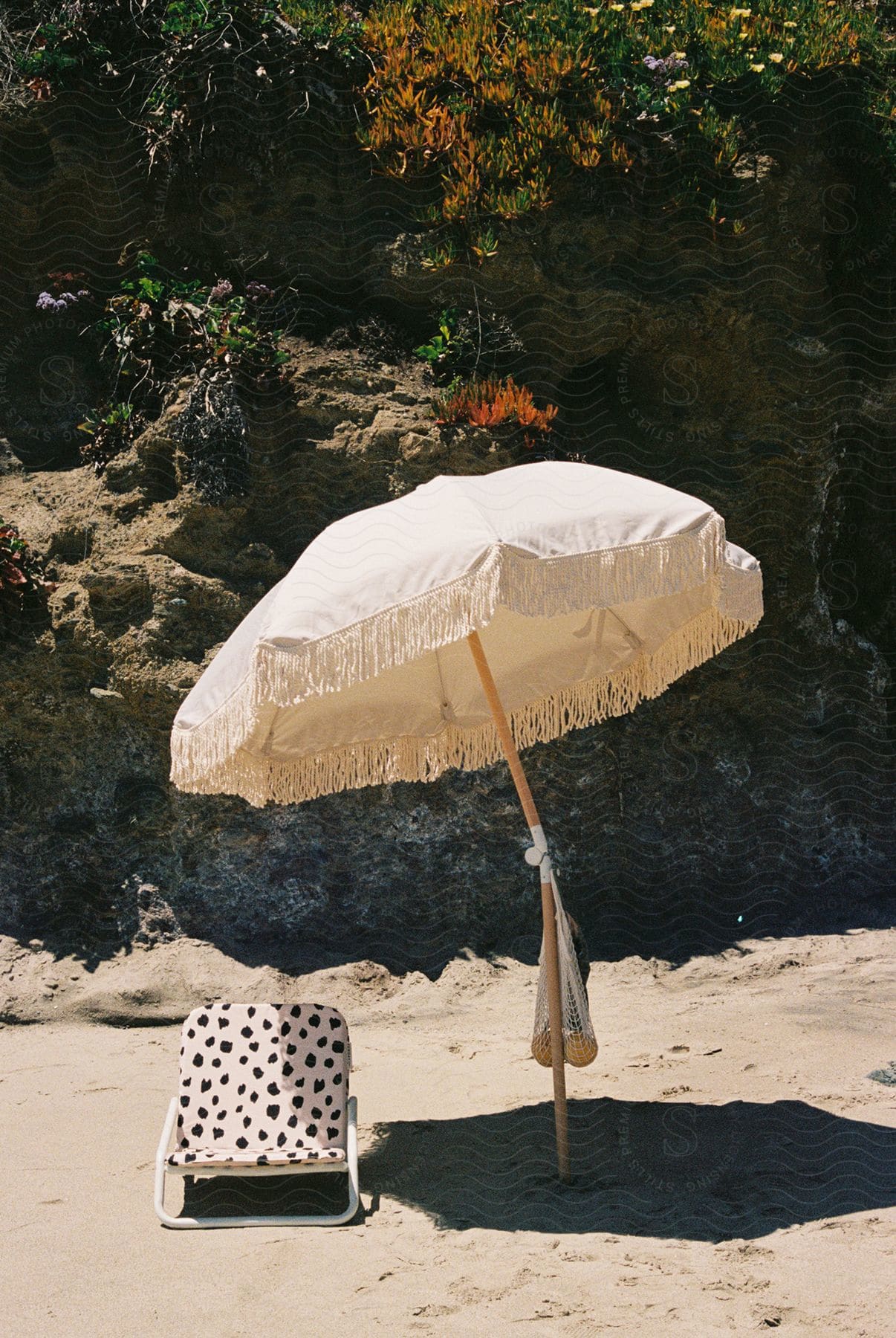 A white fringed beach umbrella beside a black and white spotted beach chair