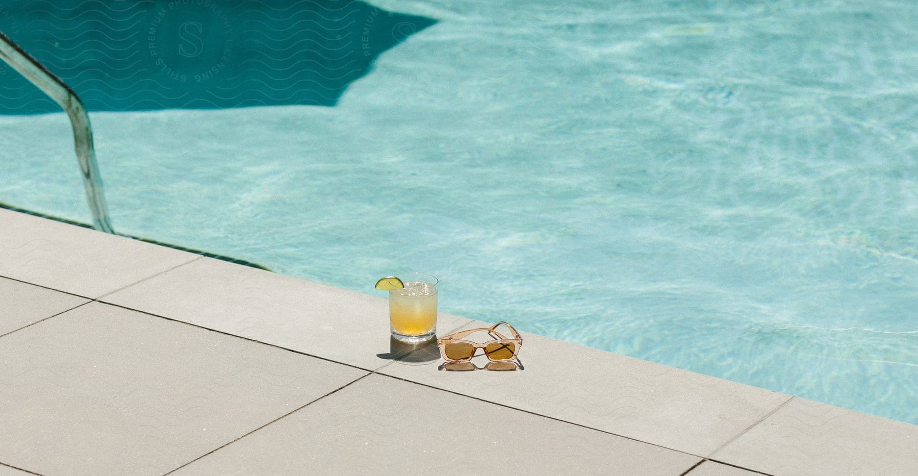 A pair of glasses and a drink by a pool