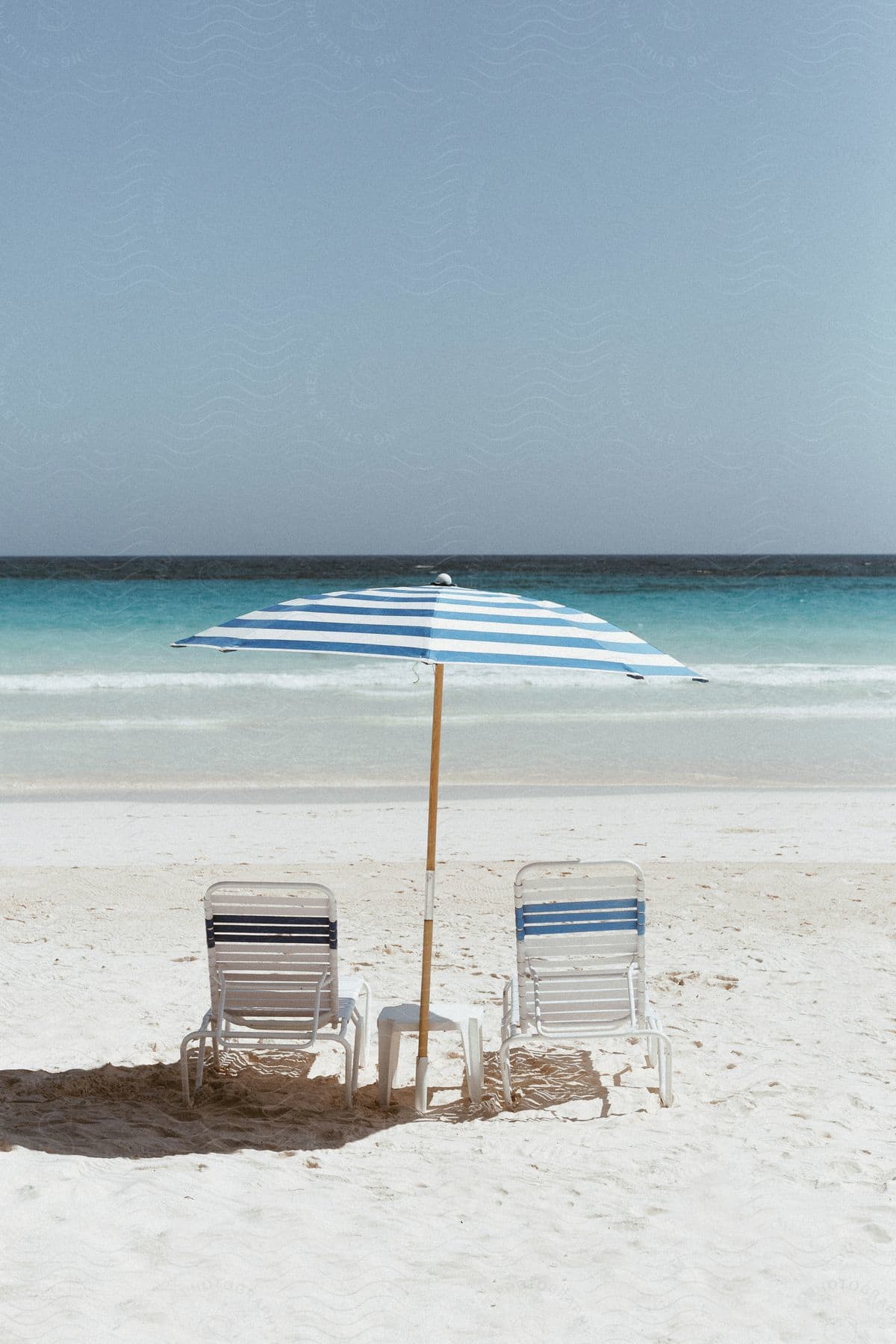 Two beach chairs and an umbrella are on the shoreline