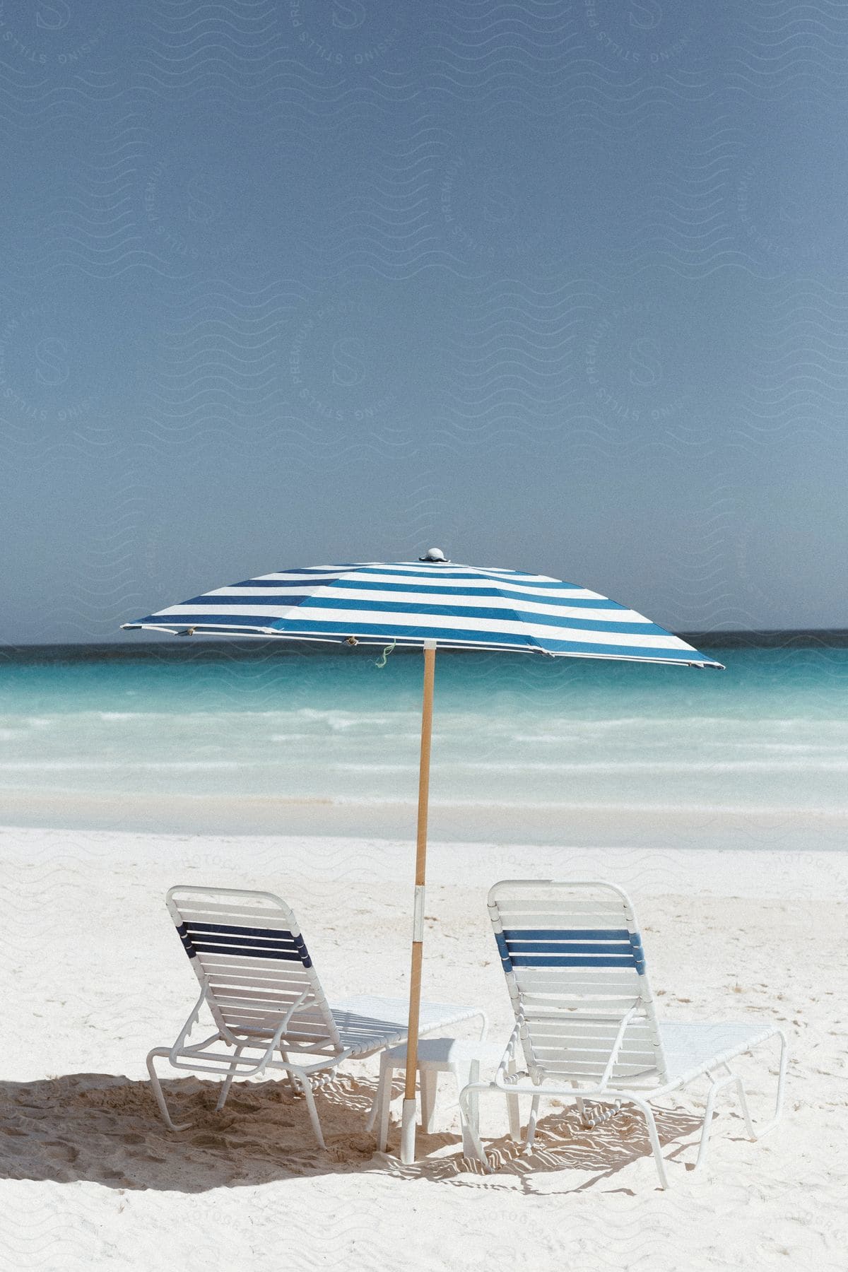 Two blue and white striped chairs and an umbrella arranged on the beach