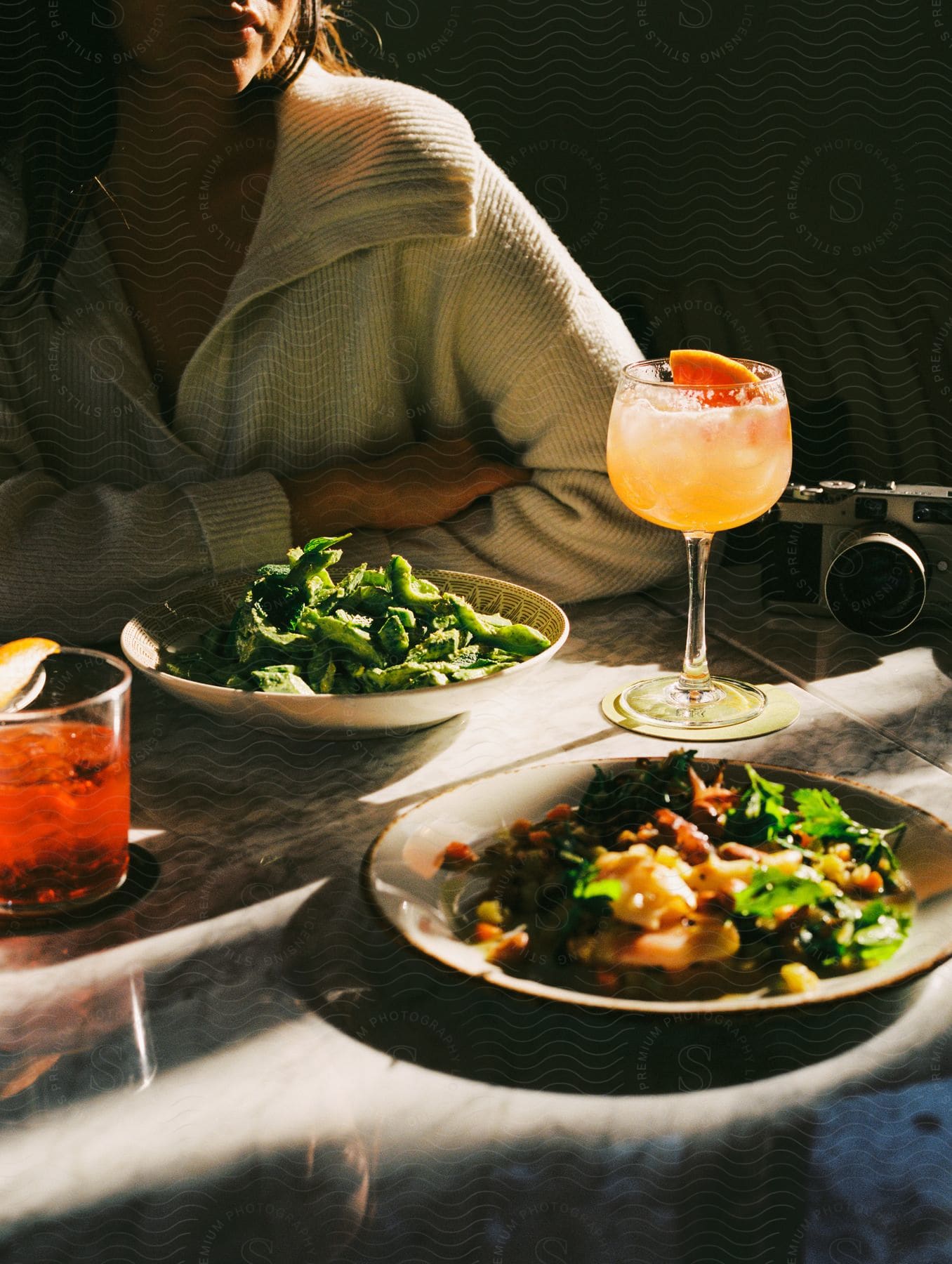 Woman wearing a white sweater sits at a table with food and drinks.