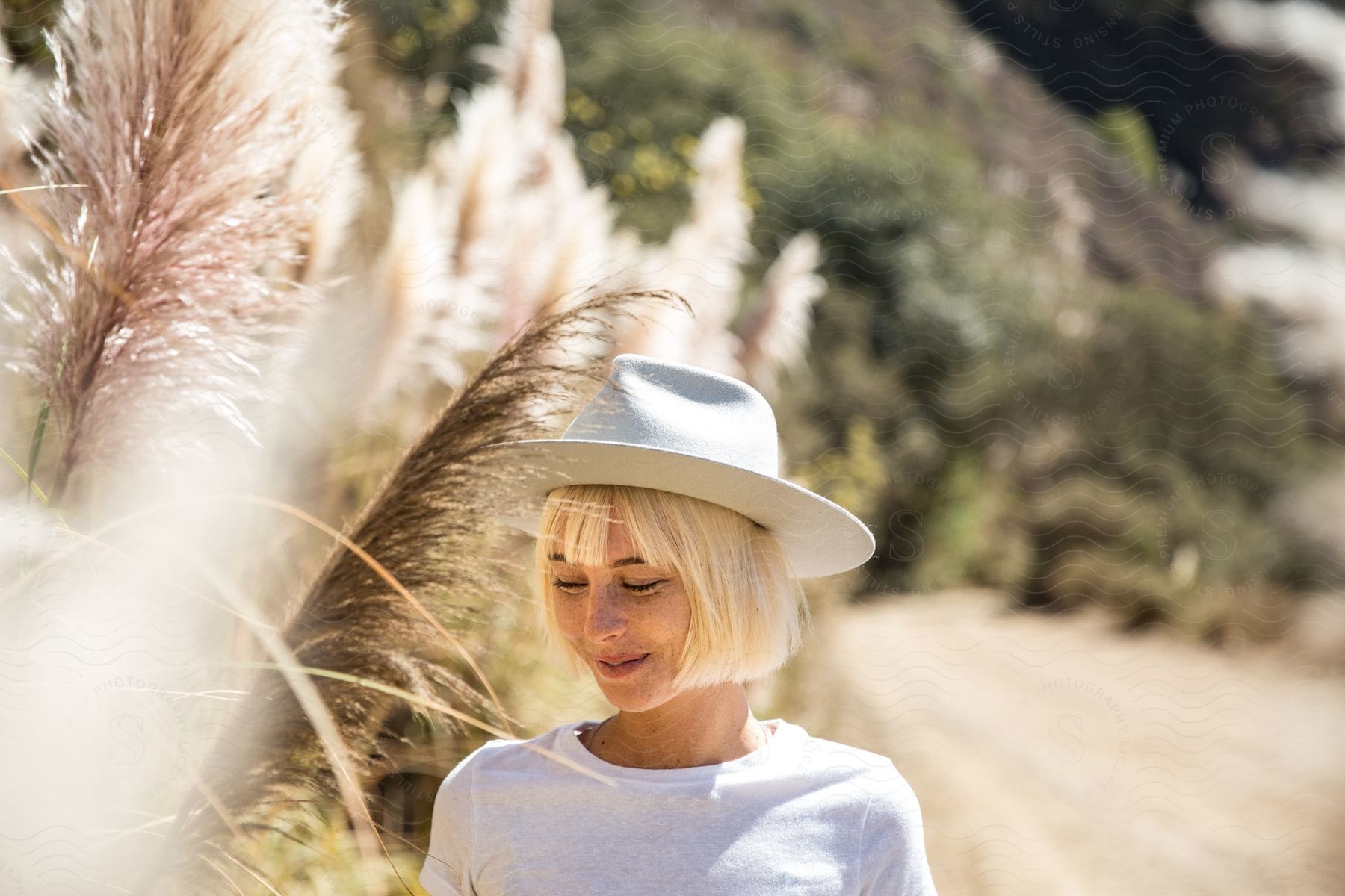 A woman with blonde hair wearing a hat and smiling surrounded by plants and reeds in nature