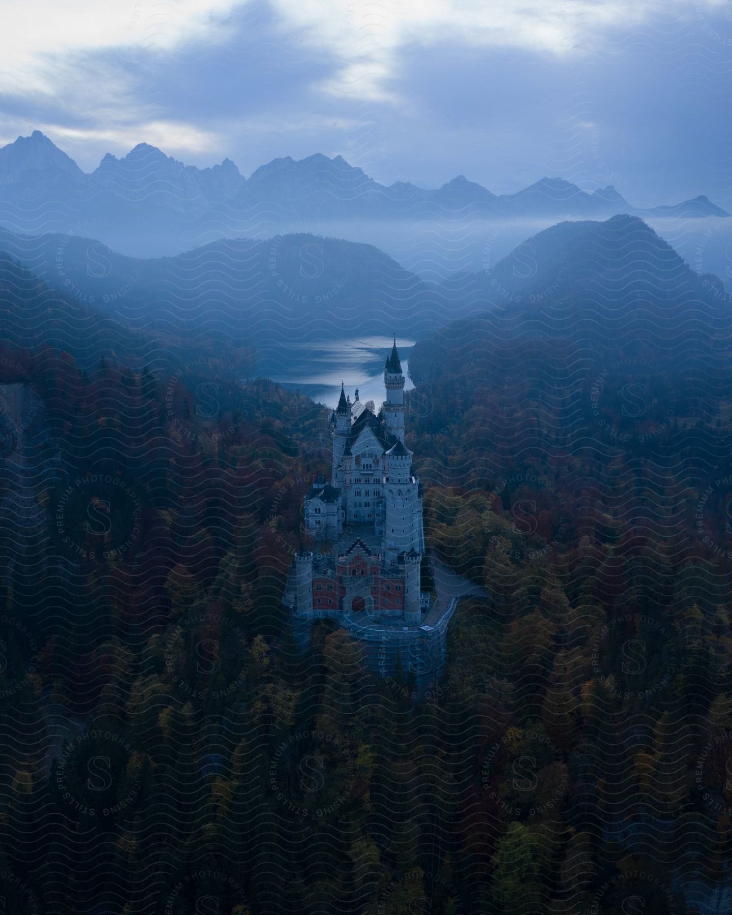 A castle surrounded by mountains and trees on a misty and cloudy day