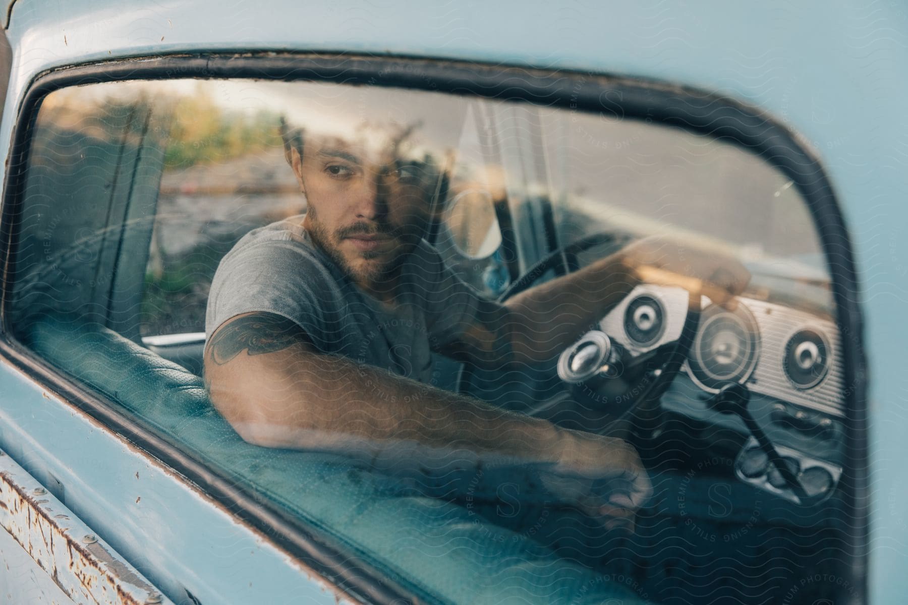 Bearded man sitting inside a truck looking out of the window with a hand on the wheel