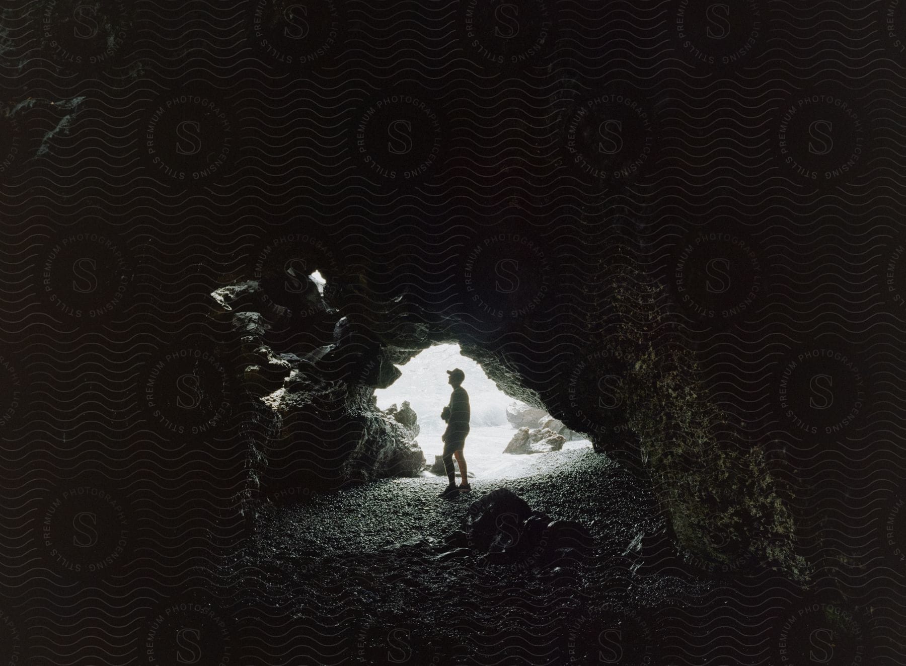 A man standing in a cave near a body of water observing the inner walls