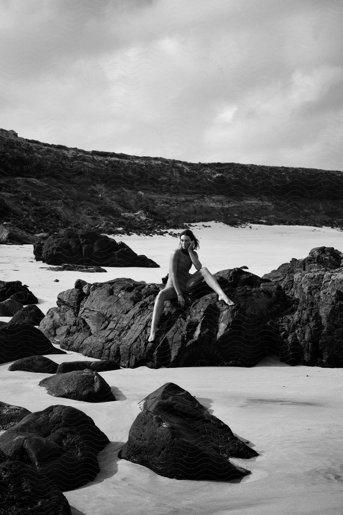 A woman sits on a rock at a rocky beach posing in a fashionable swimsuit