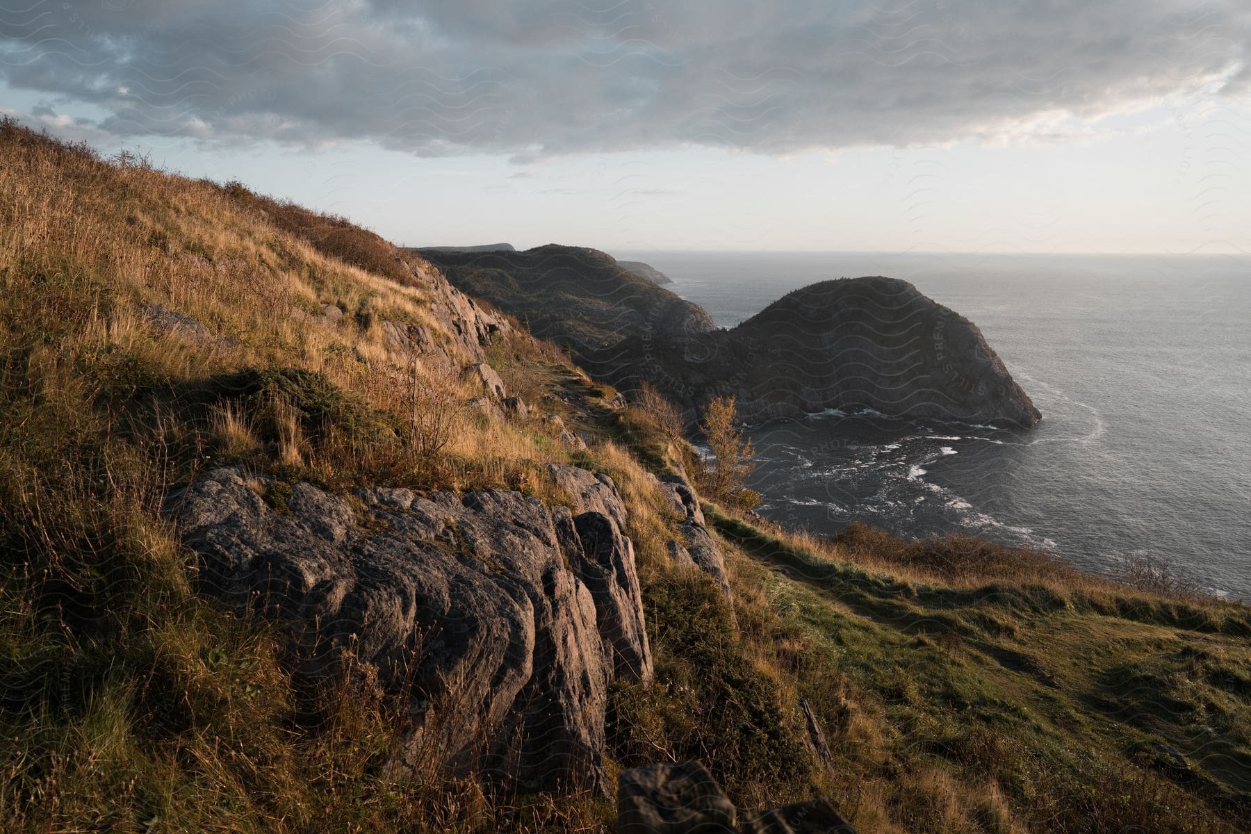 Hills and rocks next to the ocean under a cloudy sky