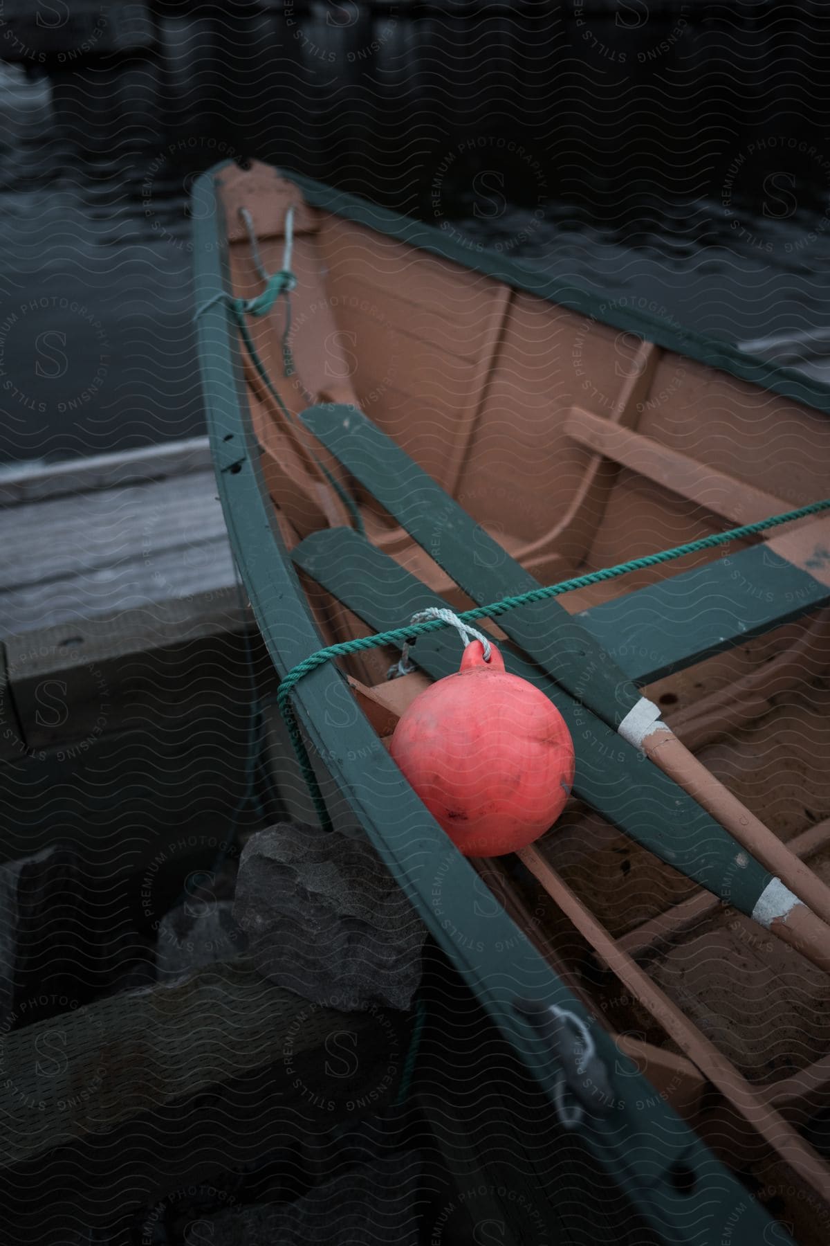 A wooden boat with paddles and a boundary buoy onboard situated at the edge of a lake