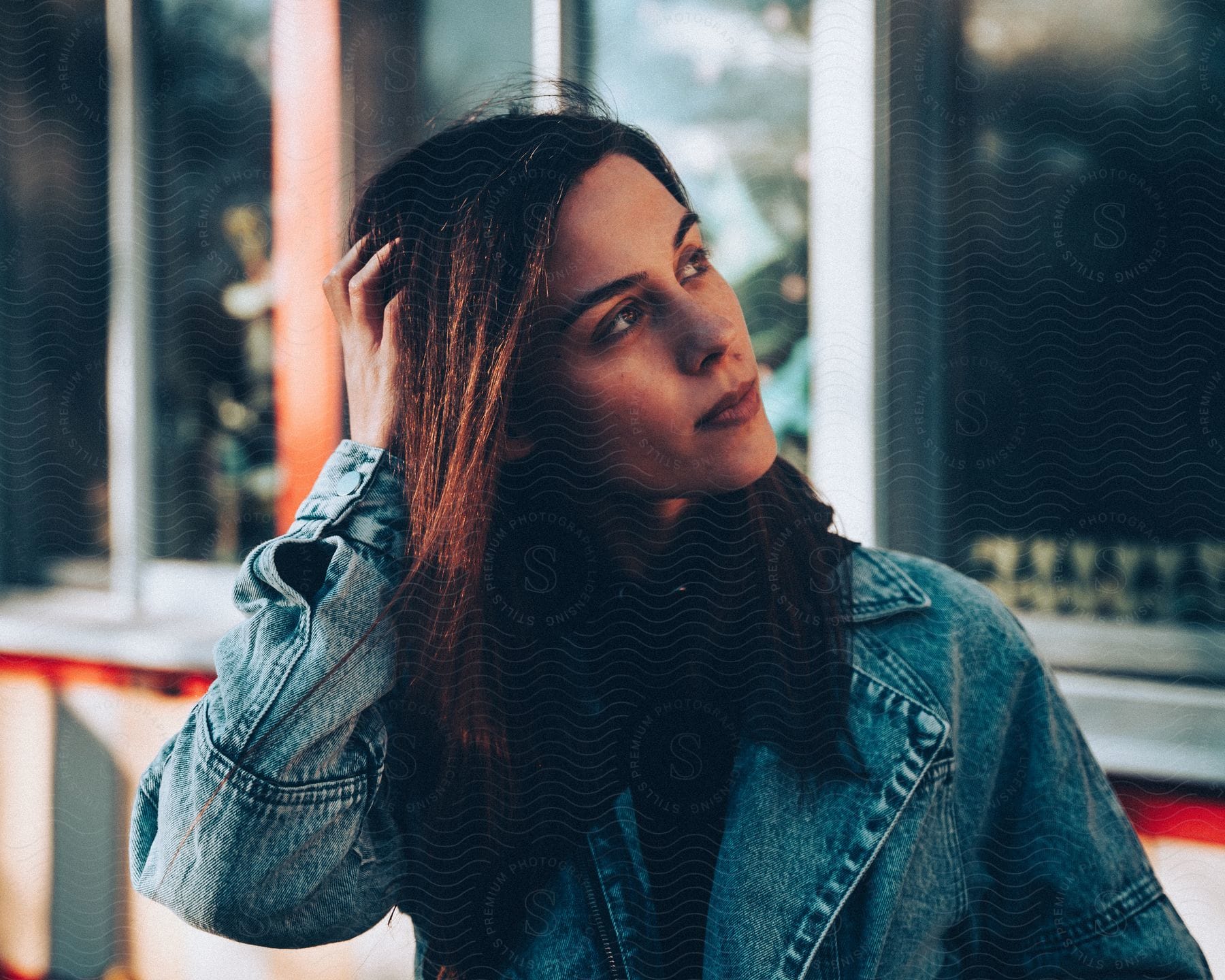 Woman with brown hair and denim jacket poses for the camera touching her hair