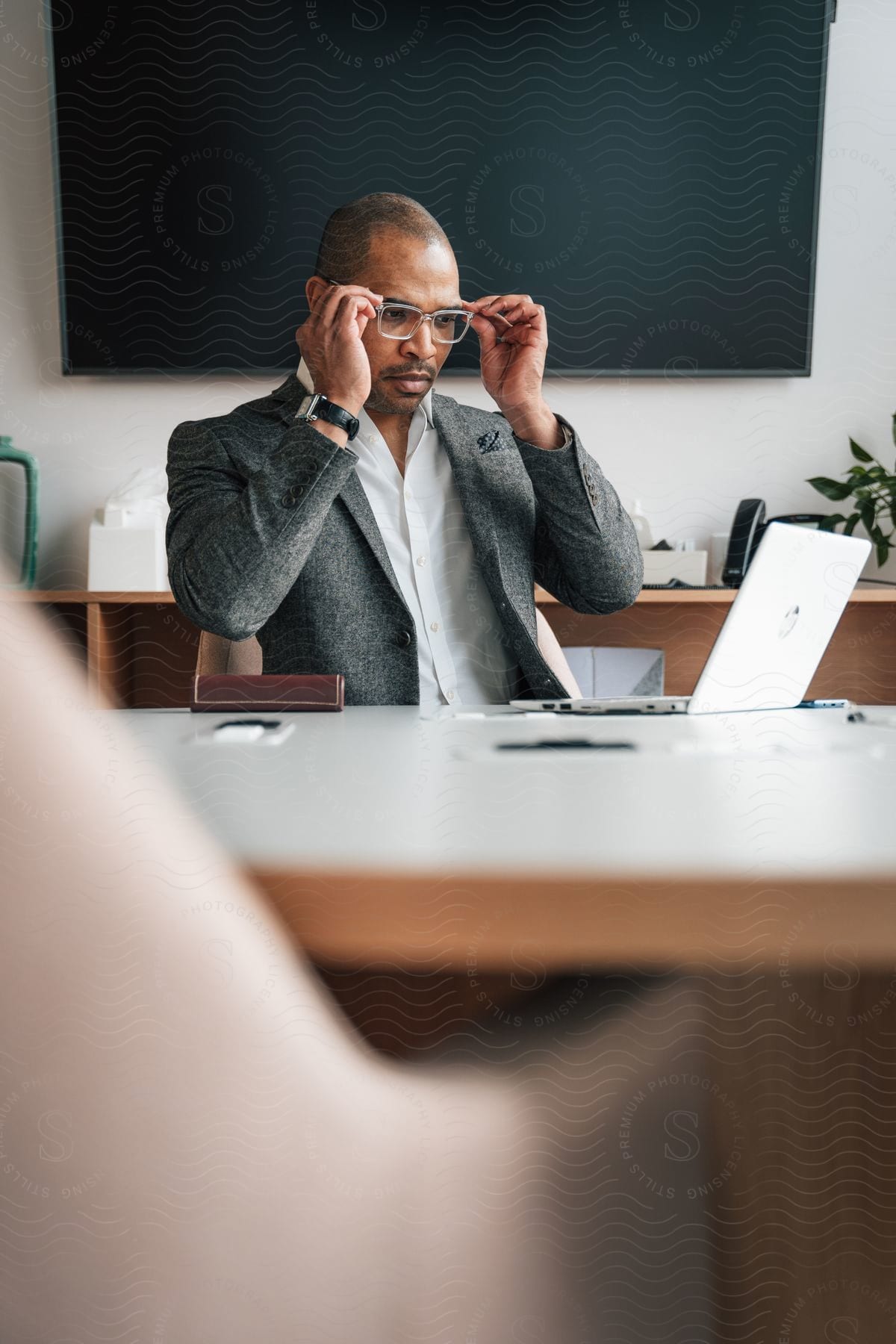 A man sitting at a desk in an office adjusting his glasses