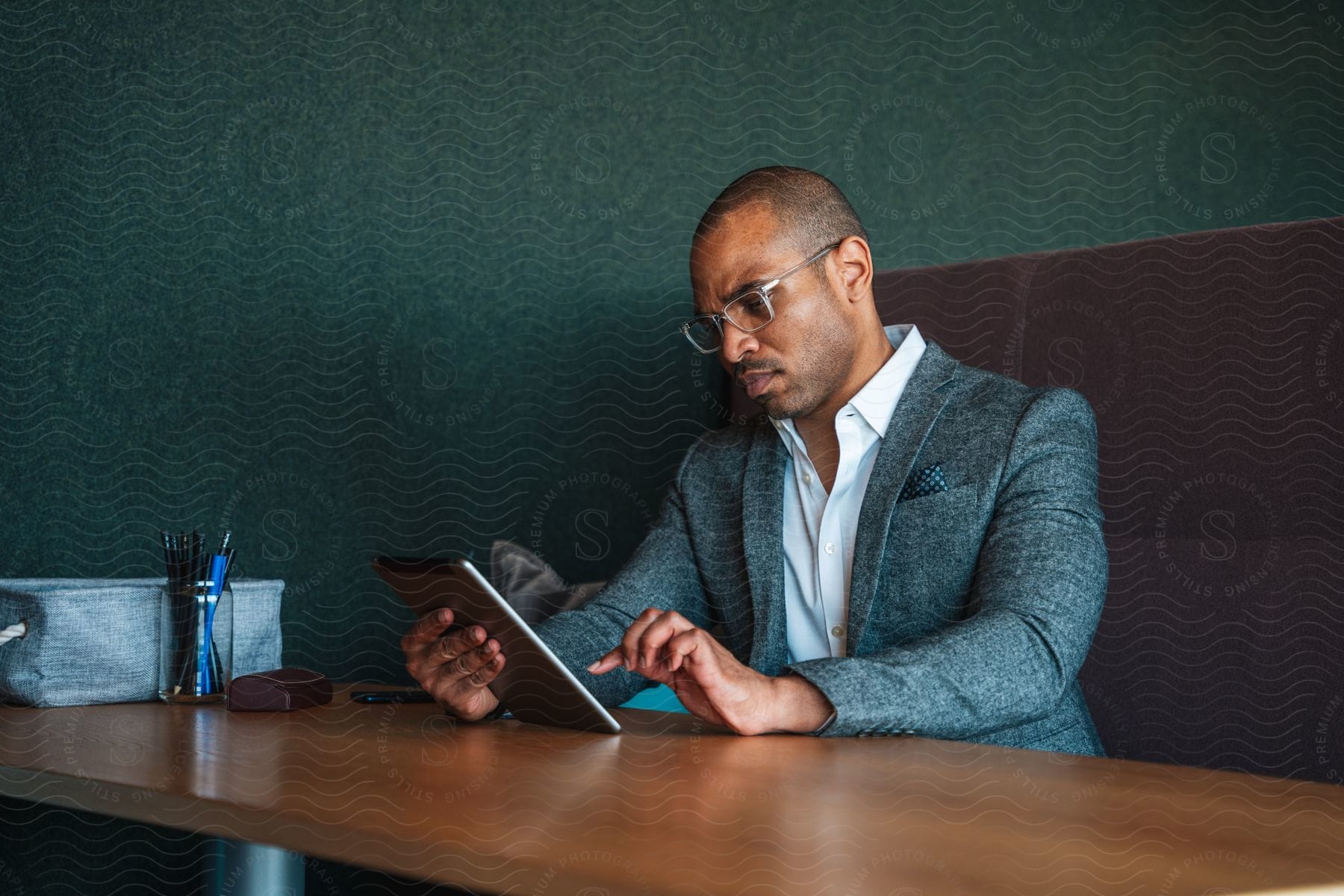 Businessman sitting at desk using tablet wearing glasses blazer jacket and white shirt