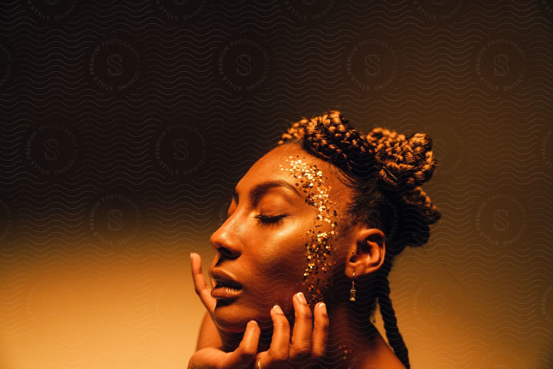 A woman with braided hair and glitter on her temple and cheek poses for a portrait