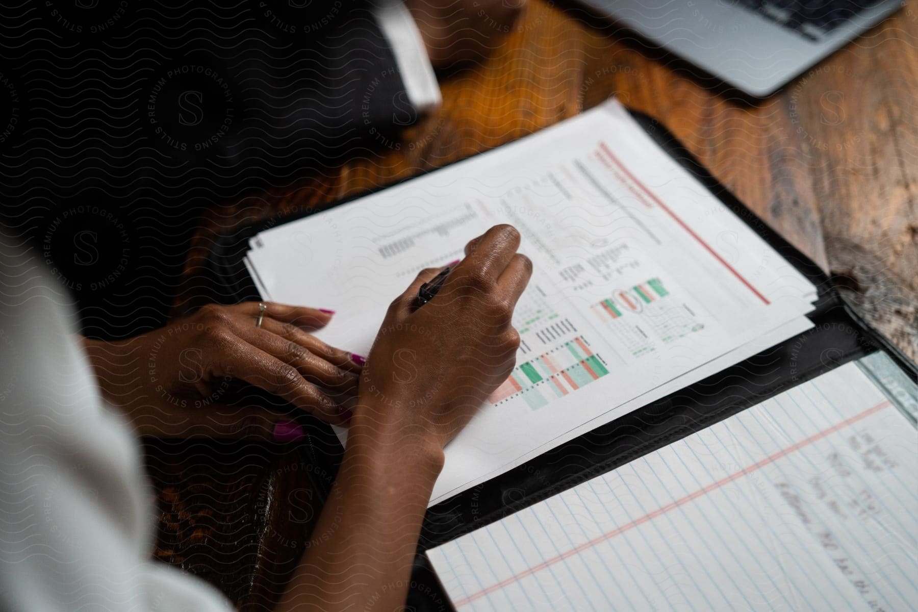 Stock photo of a woman reads and writes on a paper in a binder while a laptop sits nearby