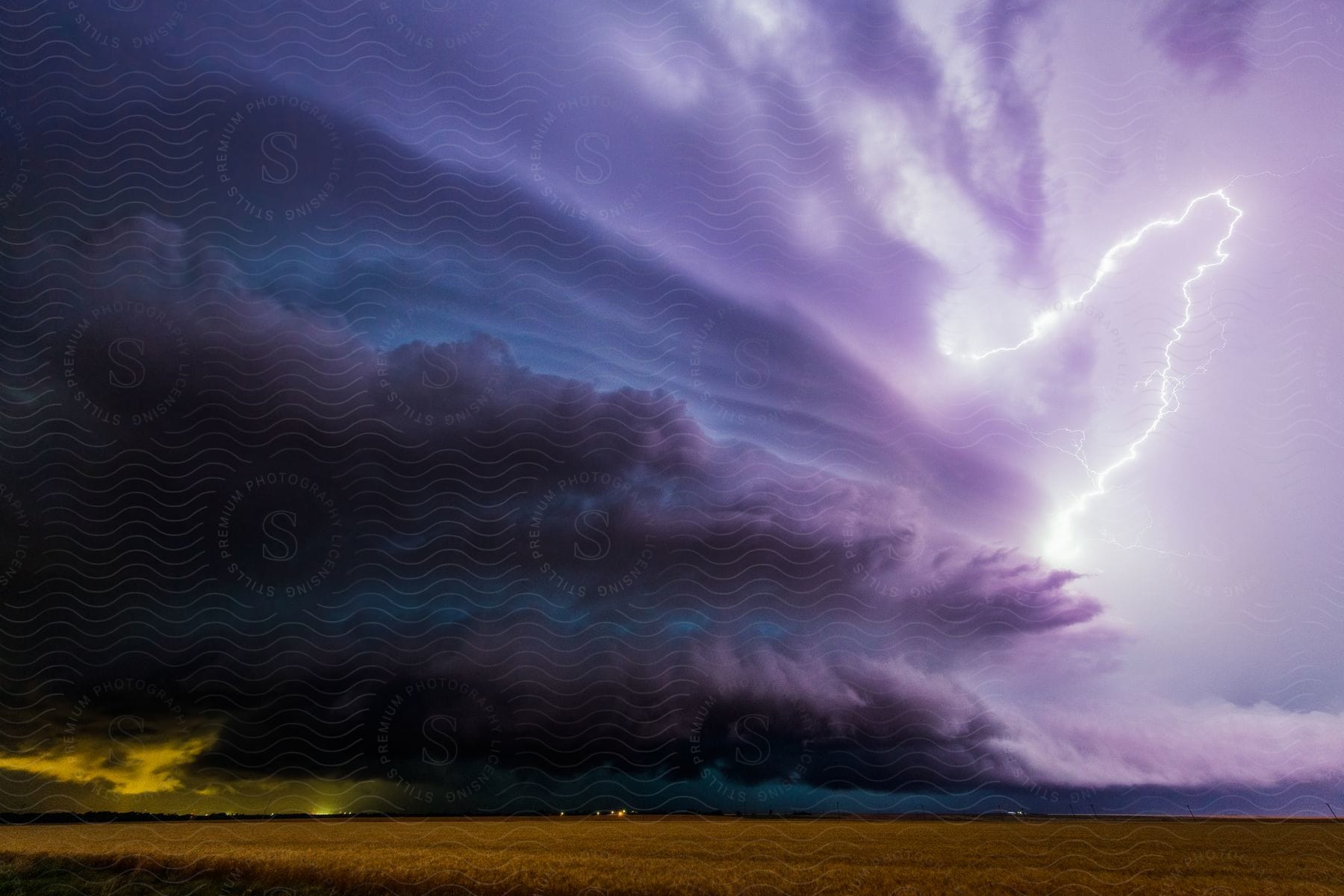 A dark supercell storm moves over rural farmland as lightning cracks the sky and rain pours down