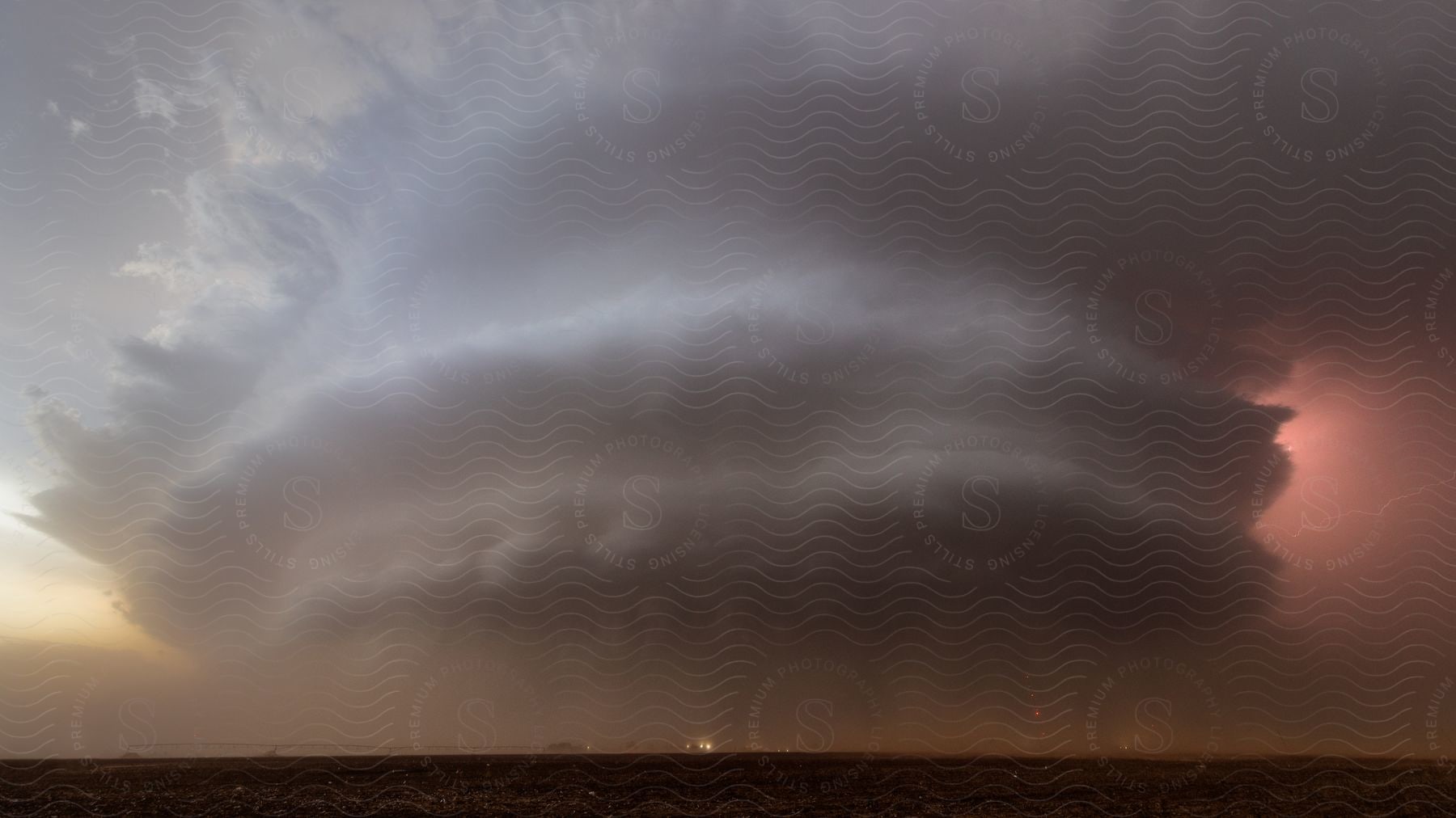 A cylindrical cloud formation in the distance dumps rain onto traffic on a flatland road