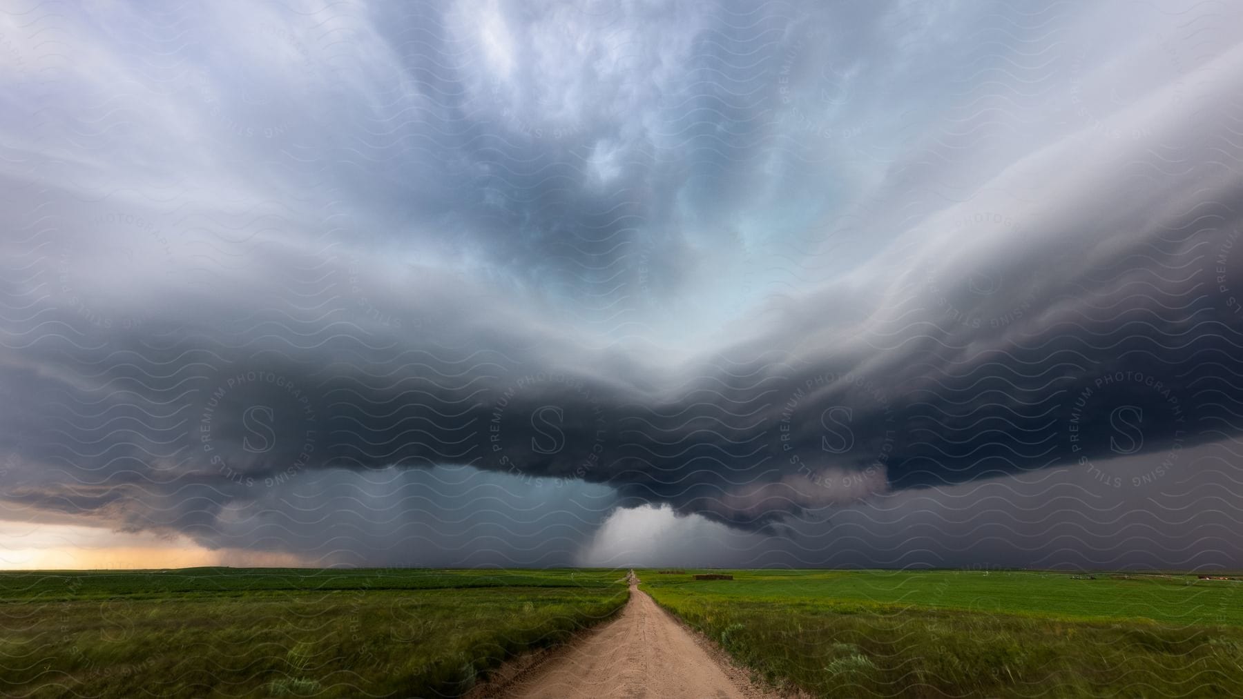 A dirt road runs through rural land as dark storm clouds hang overhead