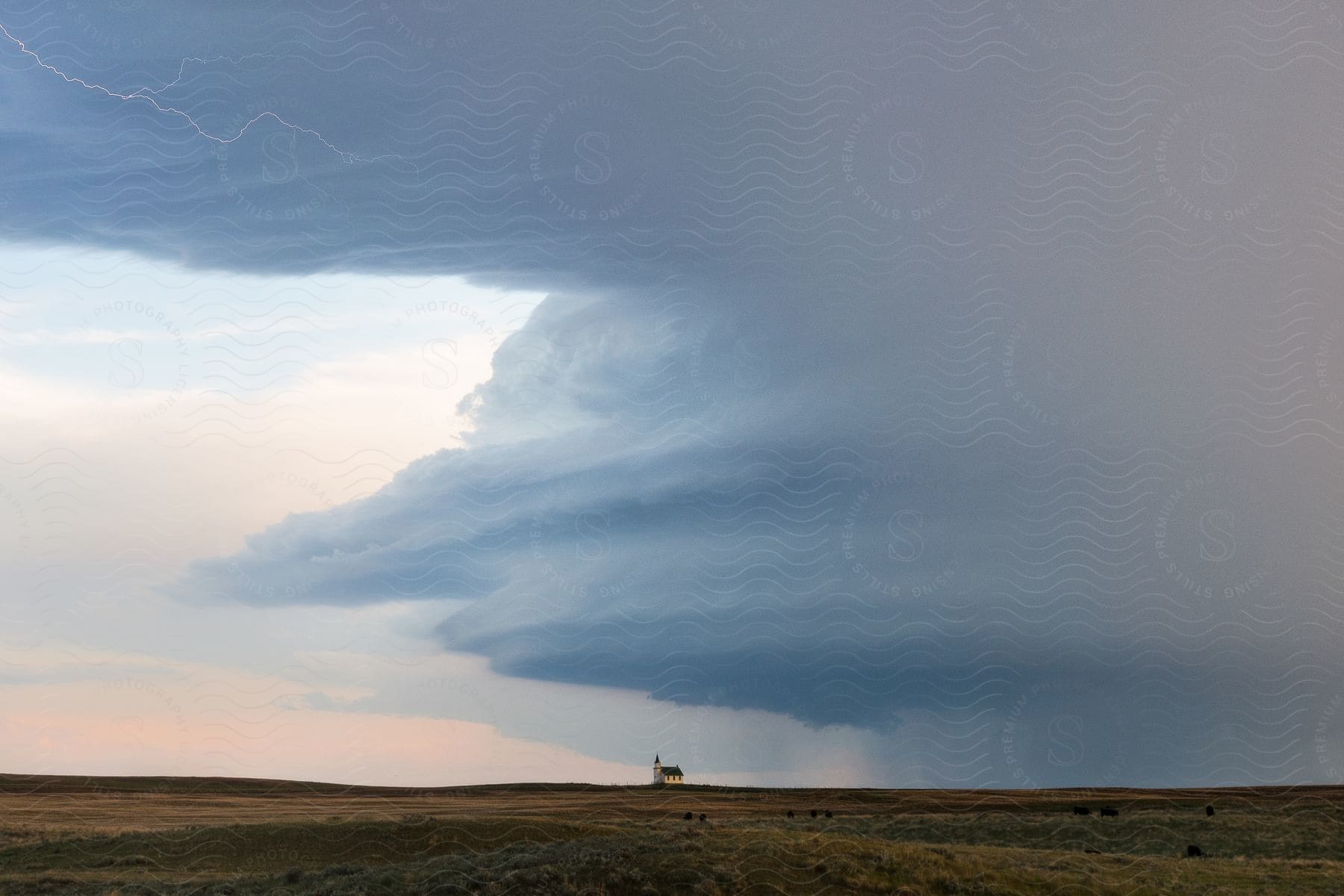 Landscape of a distant house surrounded by a vast field as dark clouds gather overhead