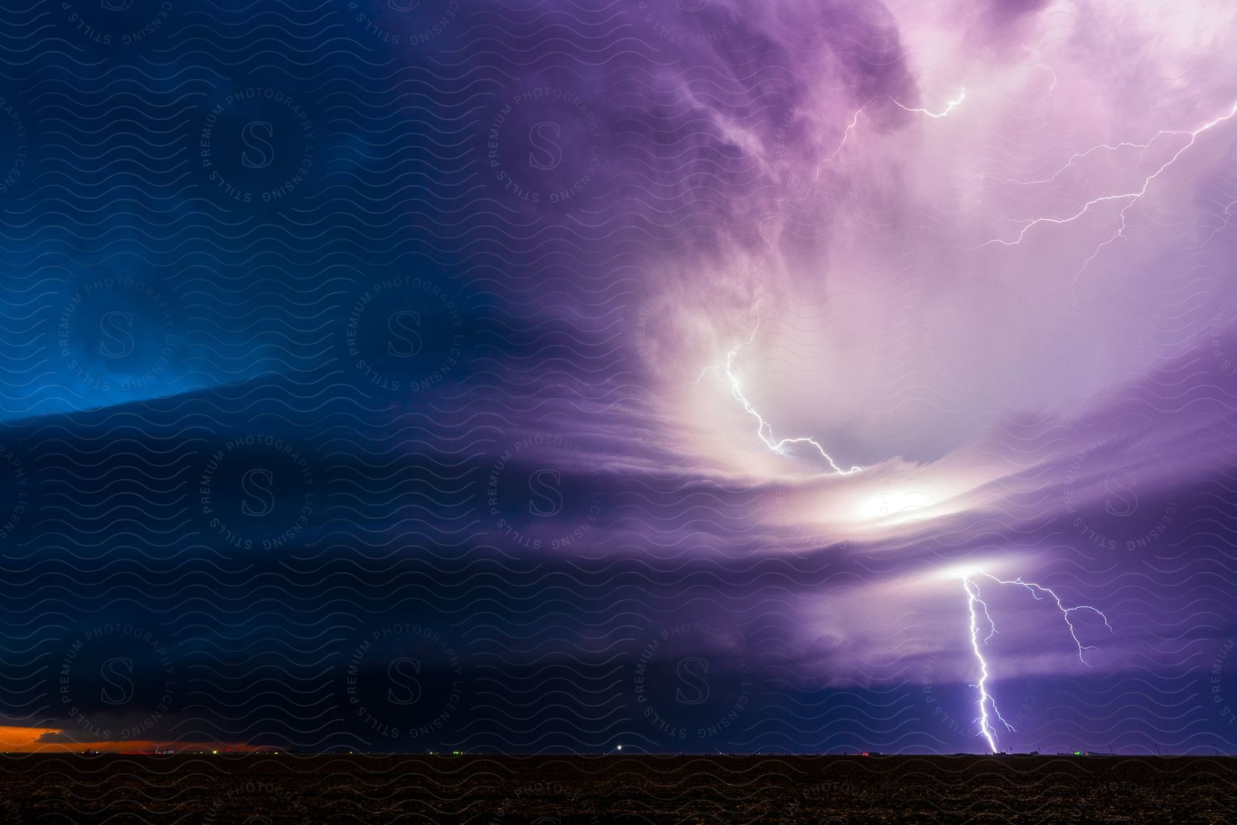 A lightning bolt strikes the ground illuminating the sky next to a storm cloud at night