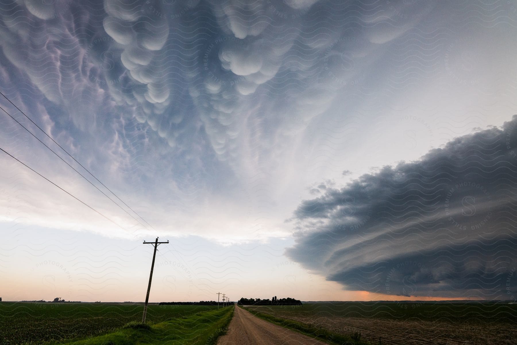 A striated supercell storm moves low over farmland near a dirt road and utility poles in arnold nebraska