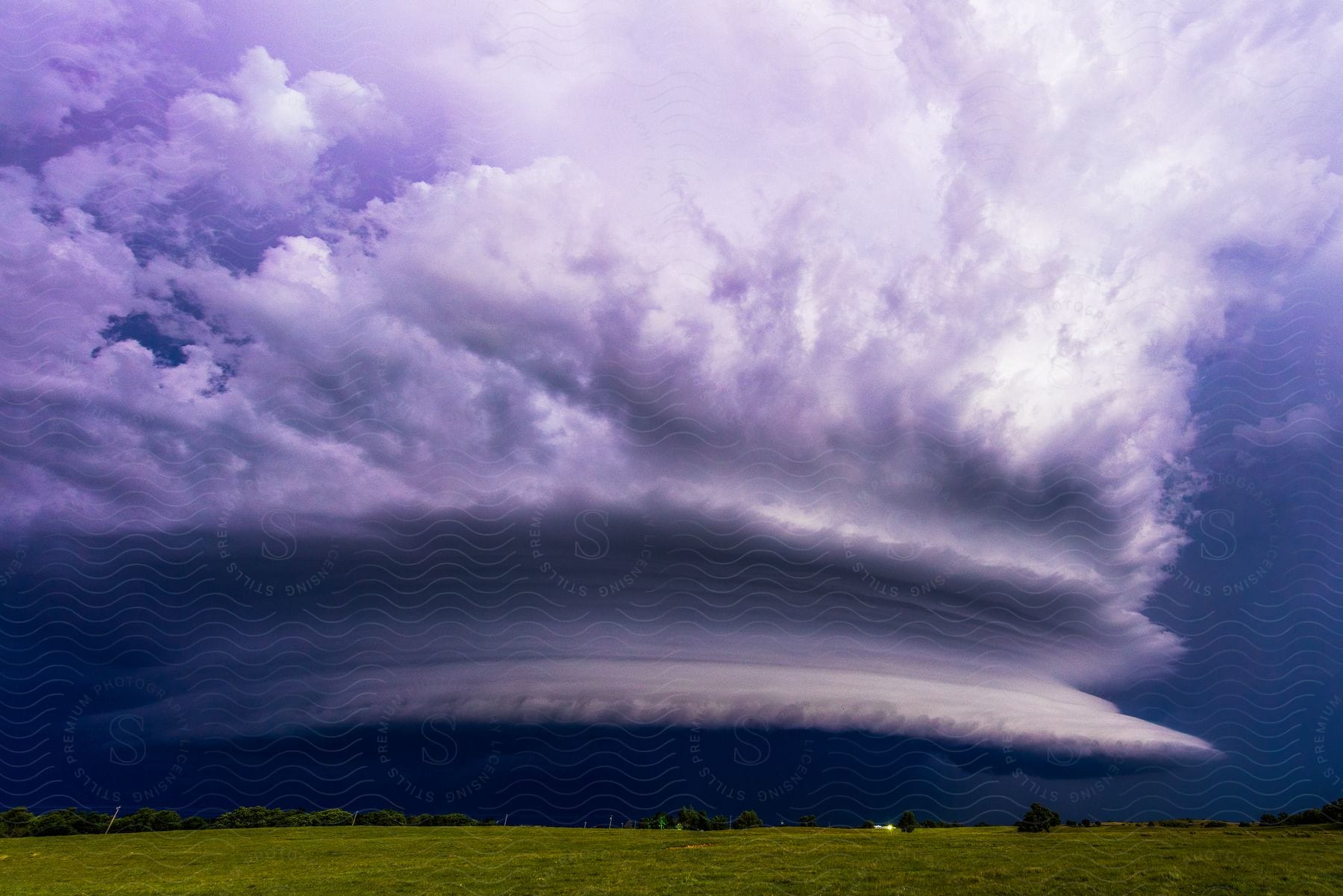 A dark supercell storm cloud hangs over rural farmland