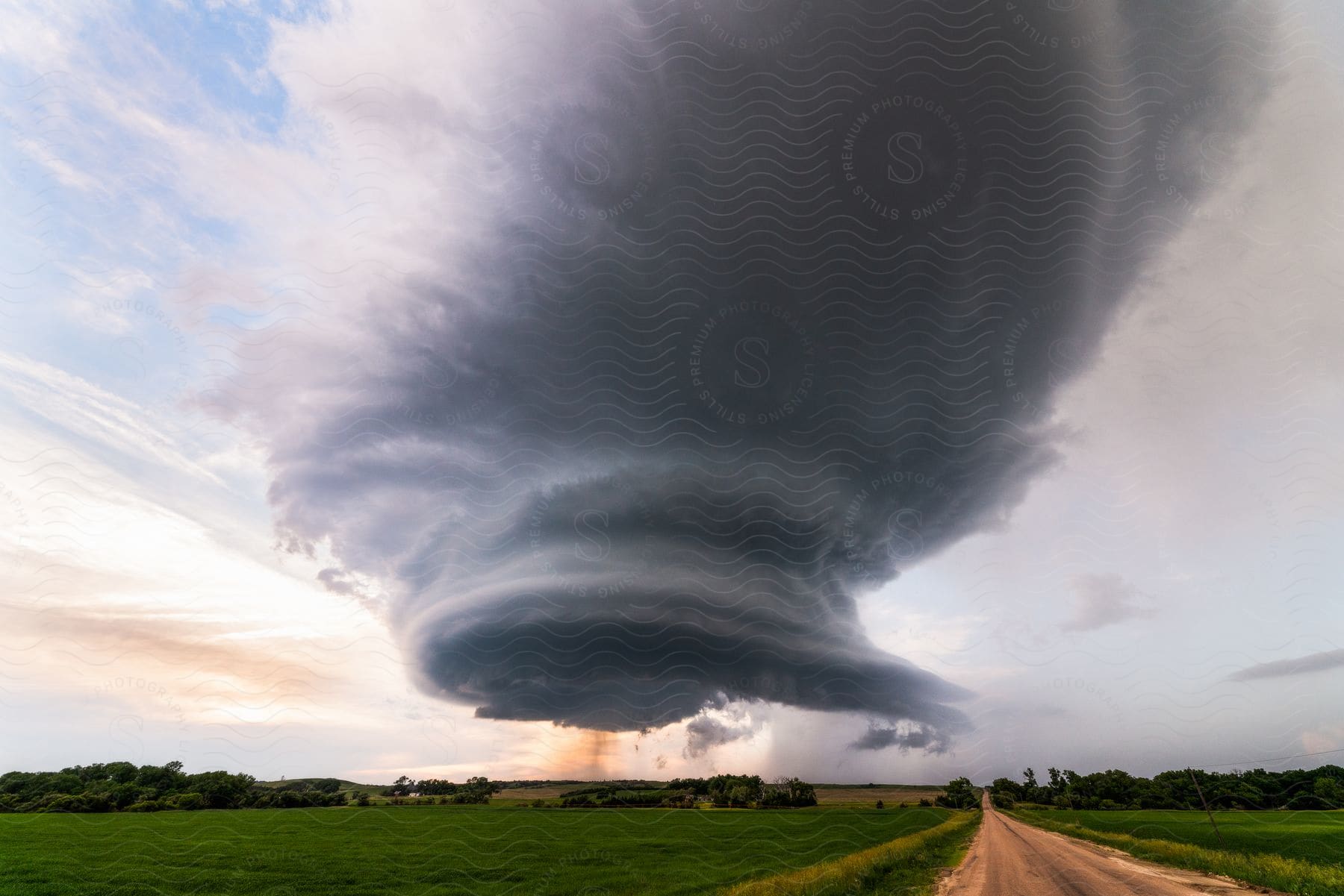 A dark supercell storm moves over houses near a rural dirt road in milburn nebraska