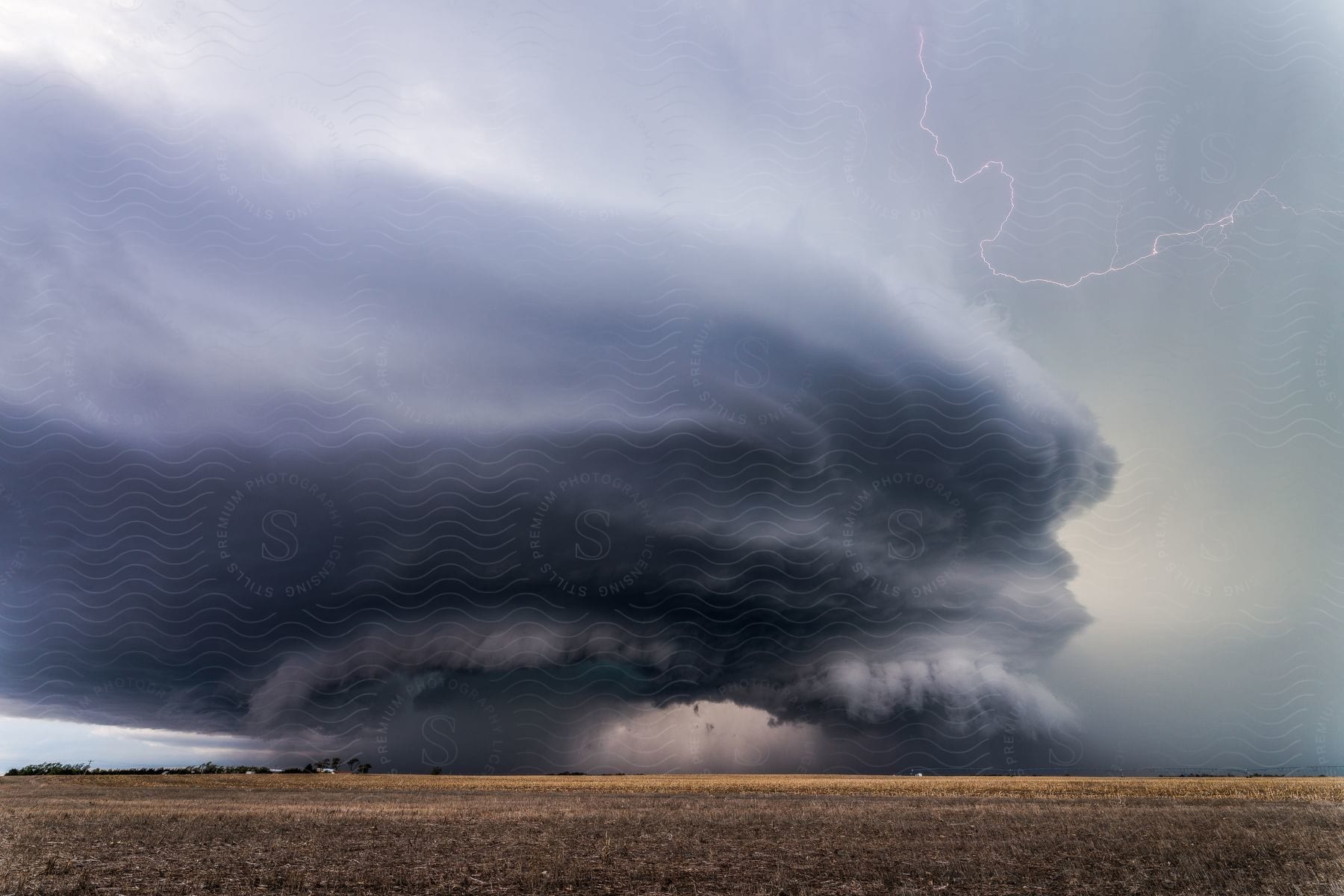 A dark supercell storm moves over farmland as lightning cracks the sky and rain pours down