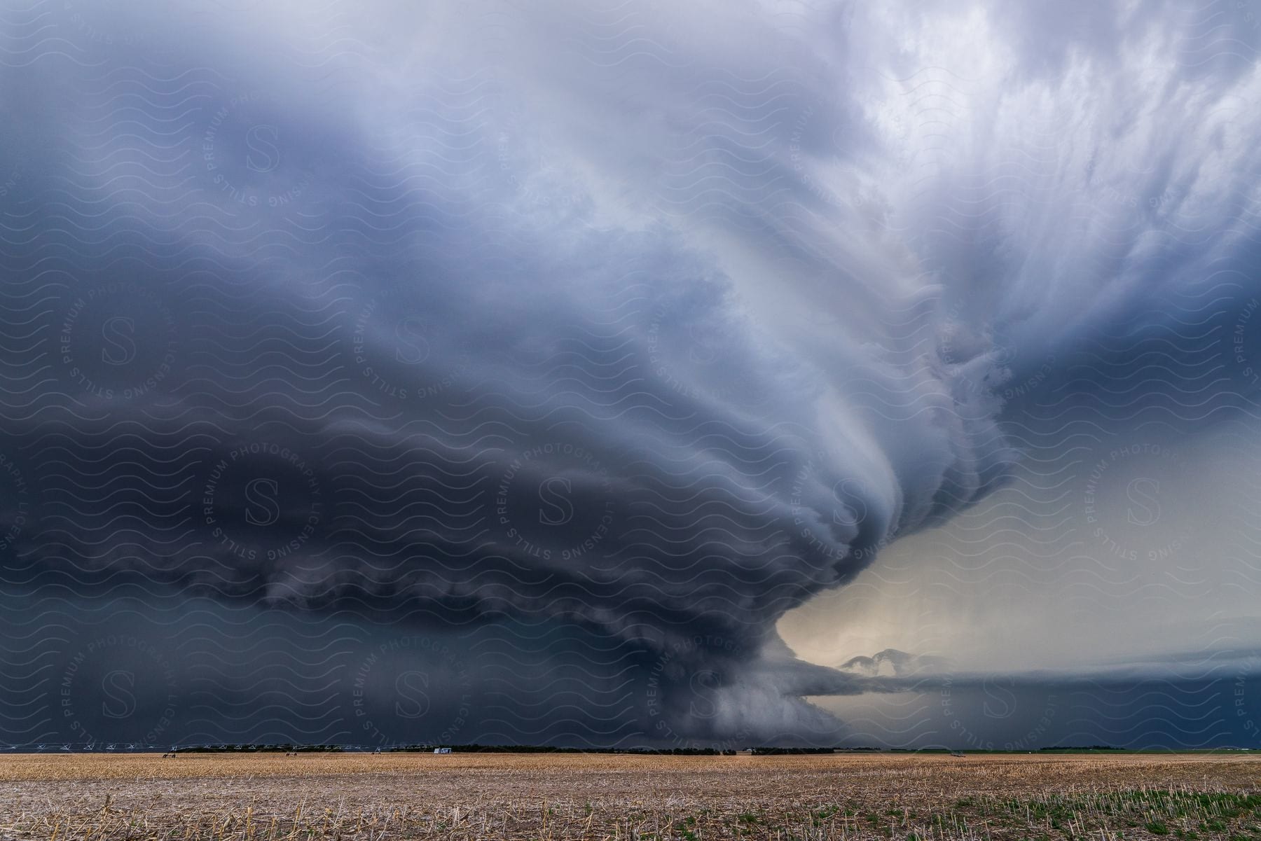A supercell storm hovers over farmland along the coast displaying impressive structure and spinning motion